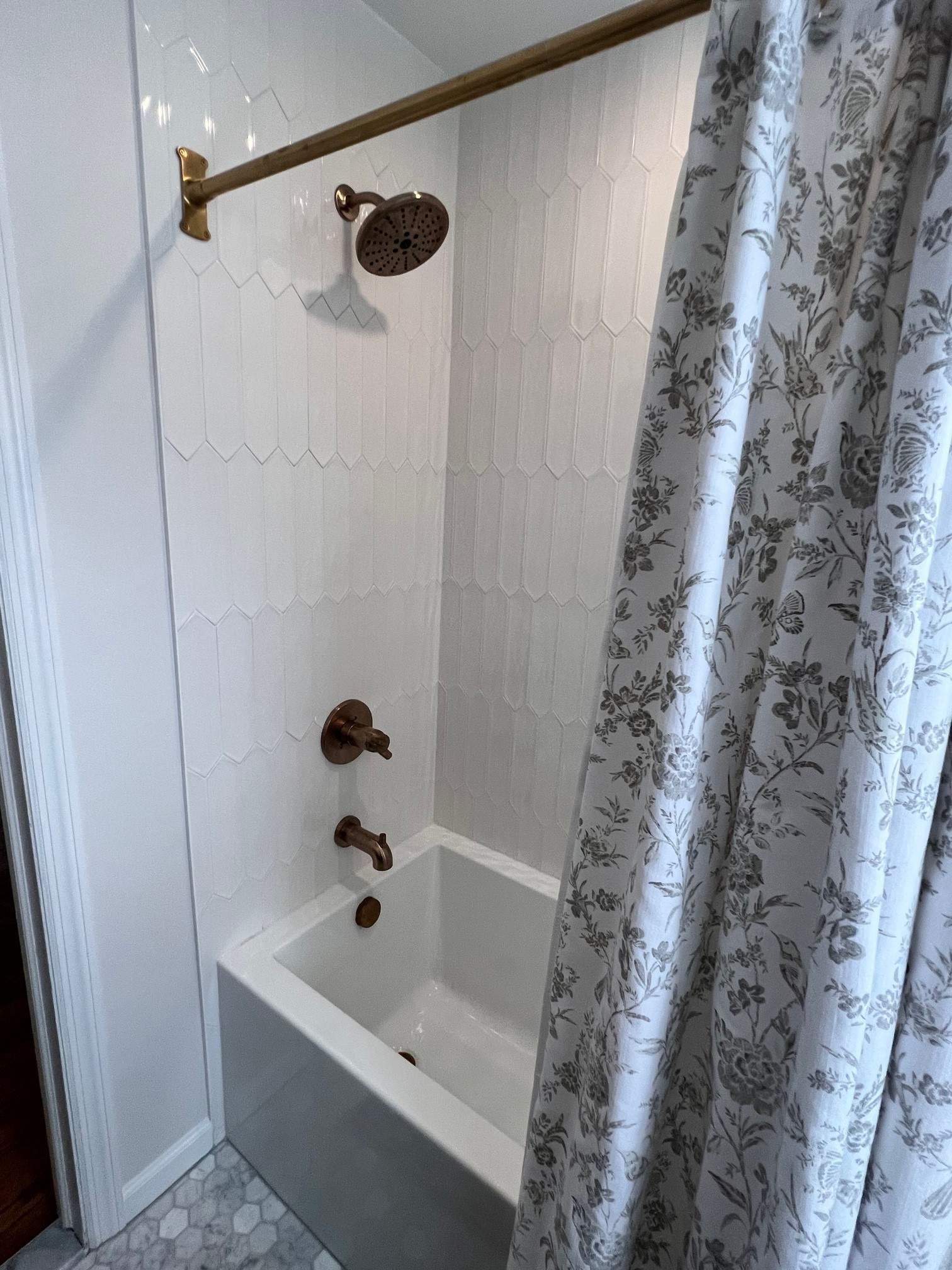 White bathroom with gold fixtures. White scalloped tile. Floral shower curtain to the right.