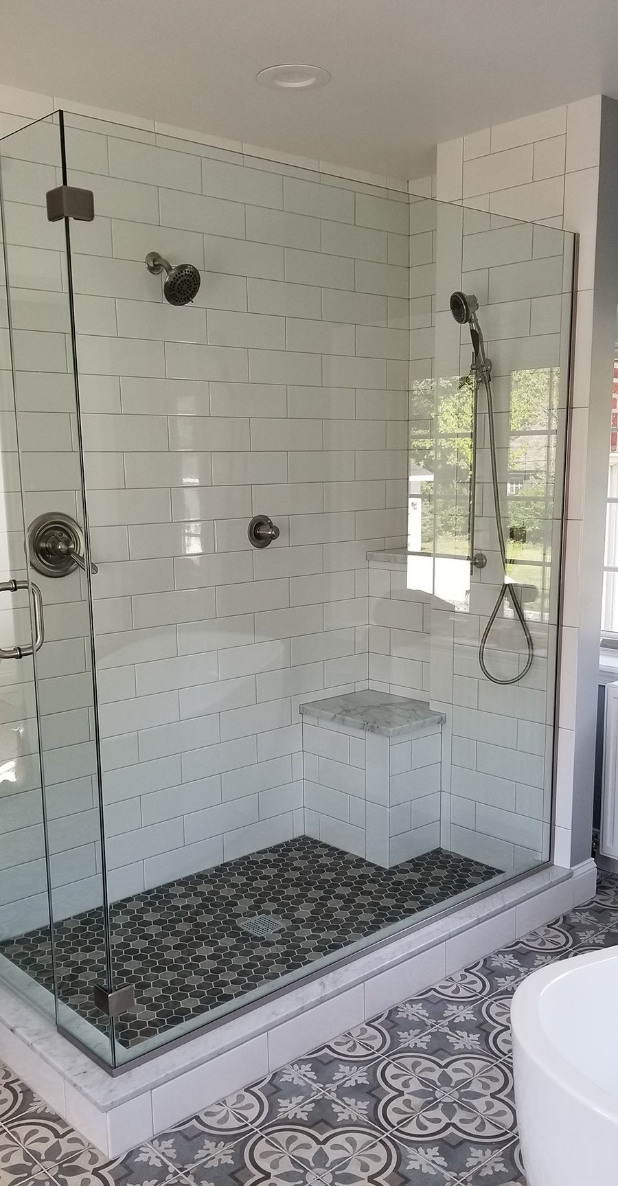 Glass shower enclosure with white tile walls, pebble floor, and chrome fixtures.
