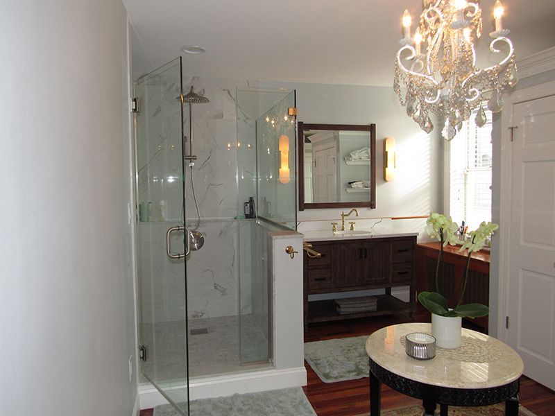 Bathroom with glass shower, dark wood vanity, chandelier, oval table, and wooden floor.