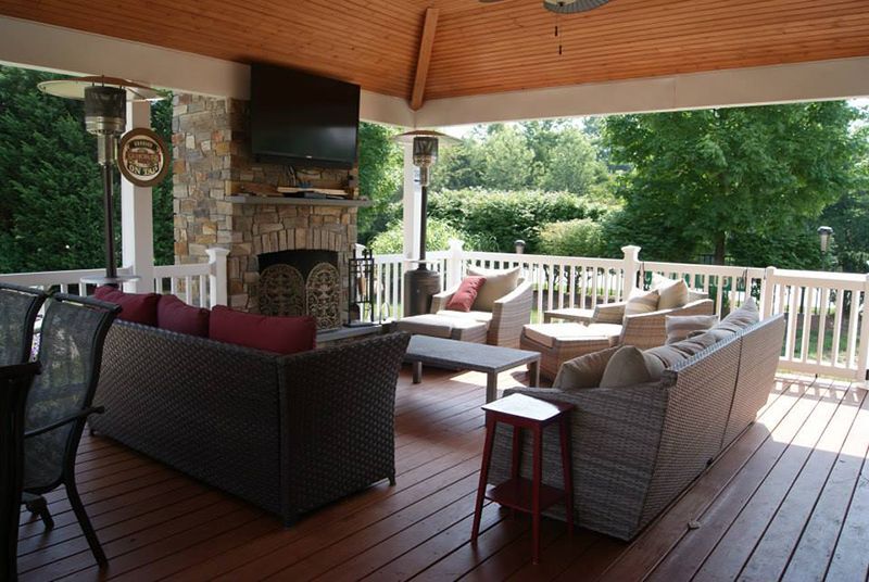 Back of a house with a covered patio, white railing, stone chimney, and a swimming pool.