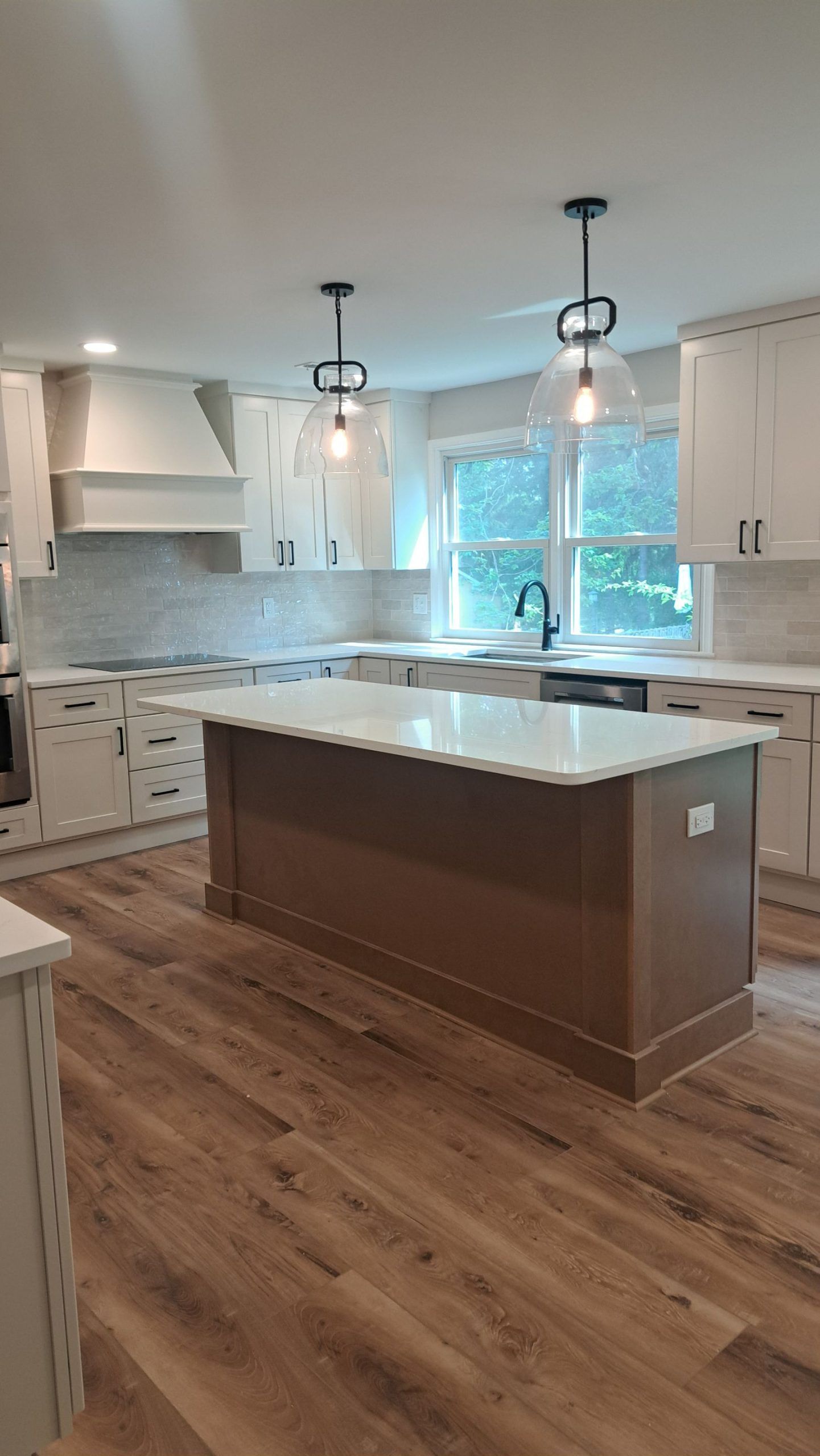 White modern kitchen with island, brown wood floor, and gold hardware.