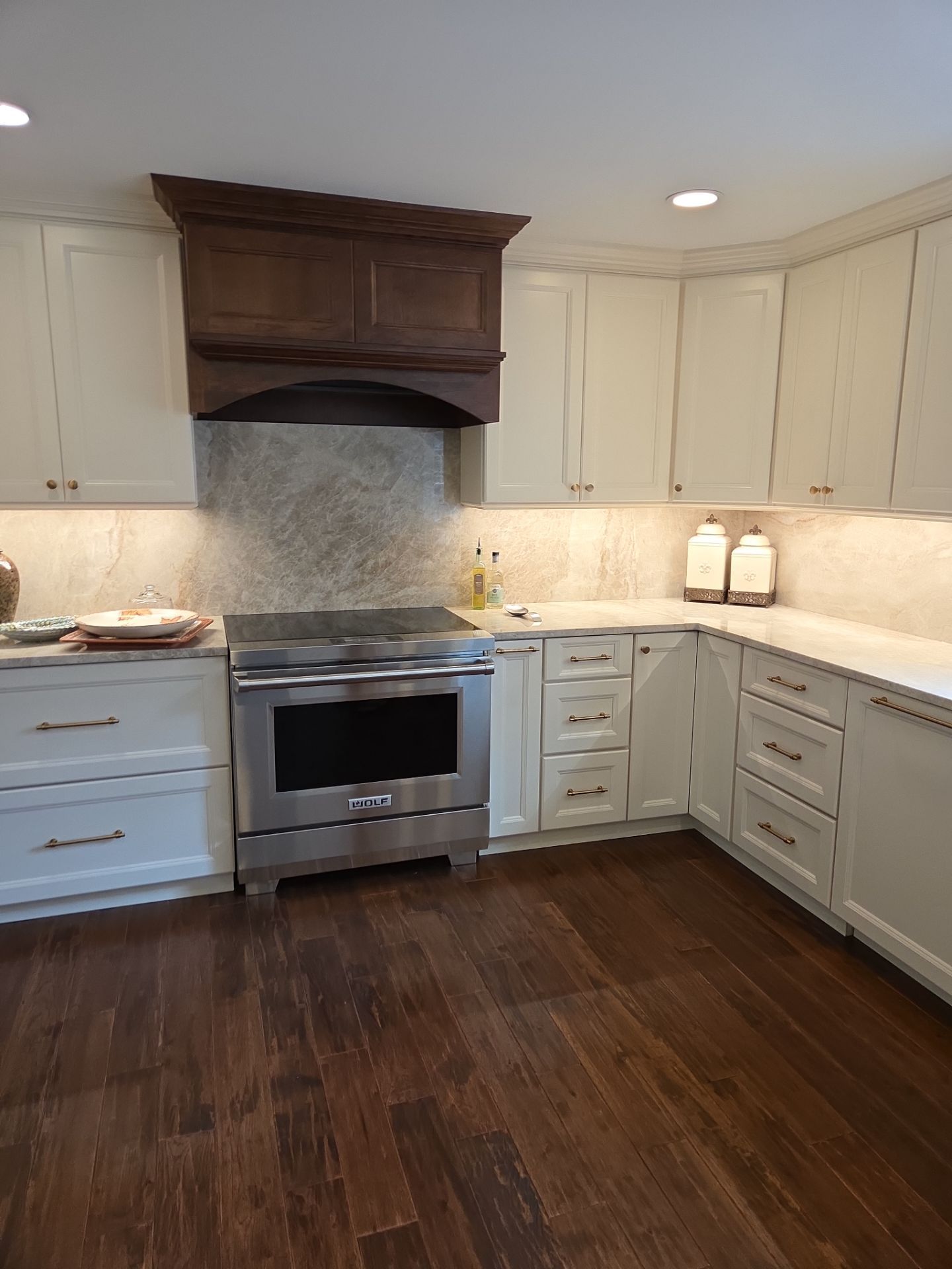 White kitchen with island, cabinets, pendant lights, and stainless steel hood.