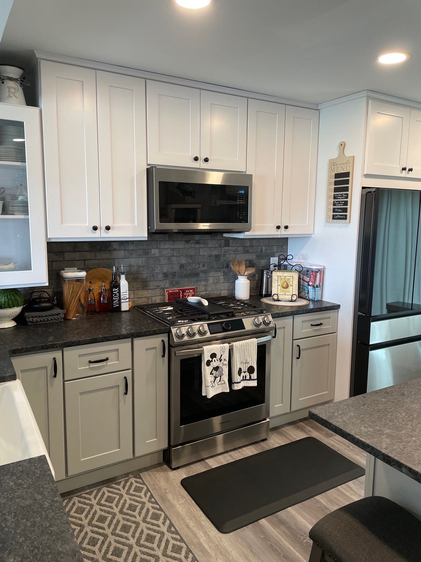Modern white kitchen with black accents, island with stools, three pendant lights, and large window.