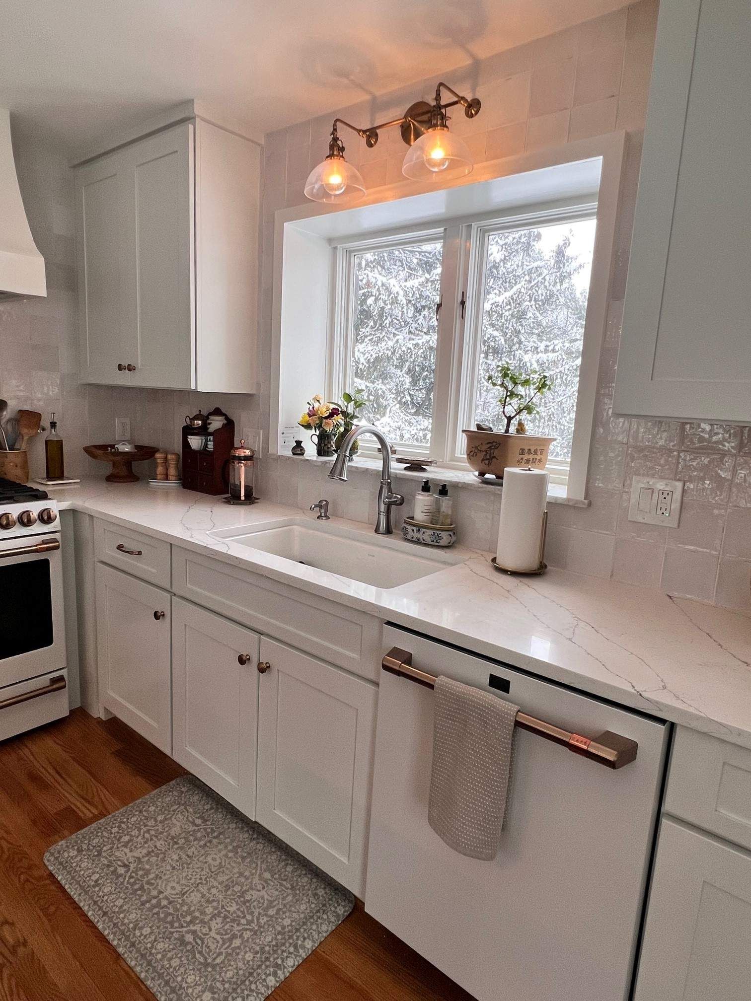 White kitchen with a snowy window view, featuring white cabinets, a farmhouse sink, and a decorative rug.