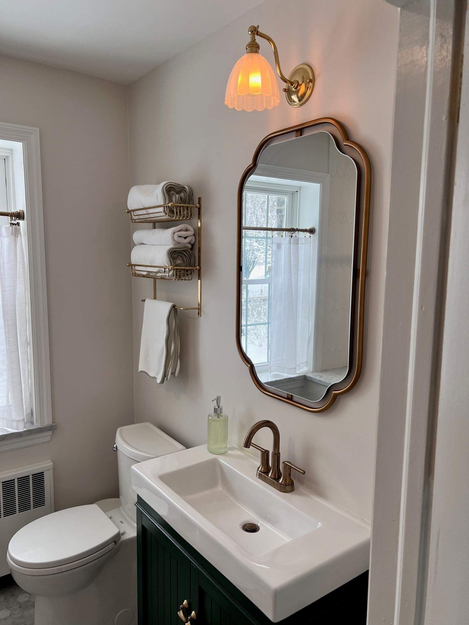 Bathroom with gold fixtures, ornate mirror, green vanity, white sink, and toilet, with a towel rack.