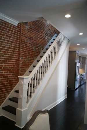 Staircase with white railing, black steps, exposed brick wall, and dark wood floor.