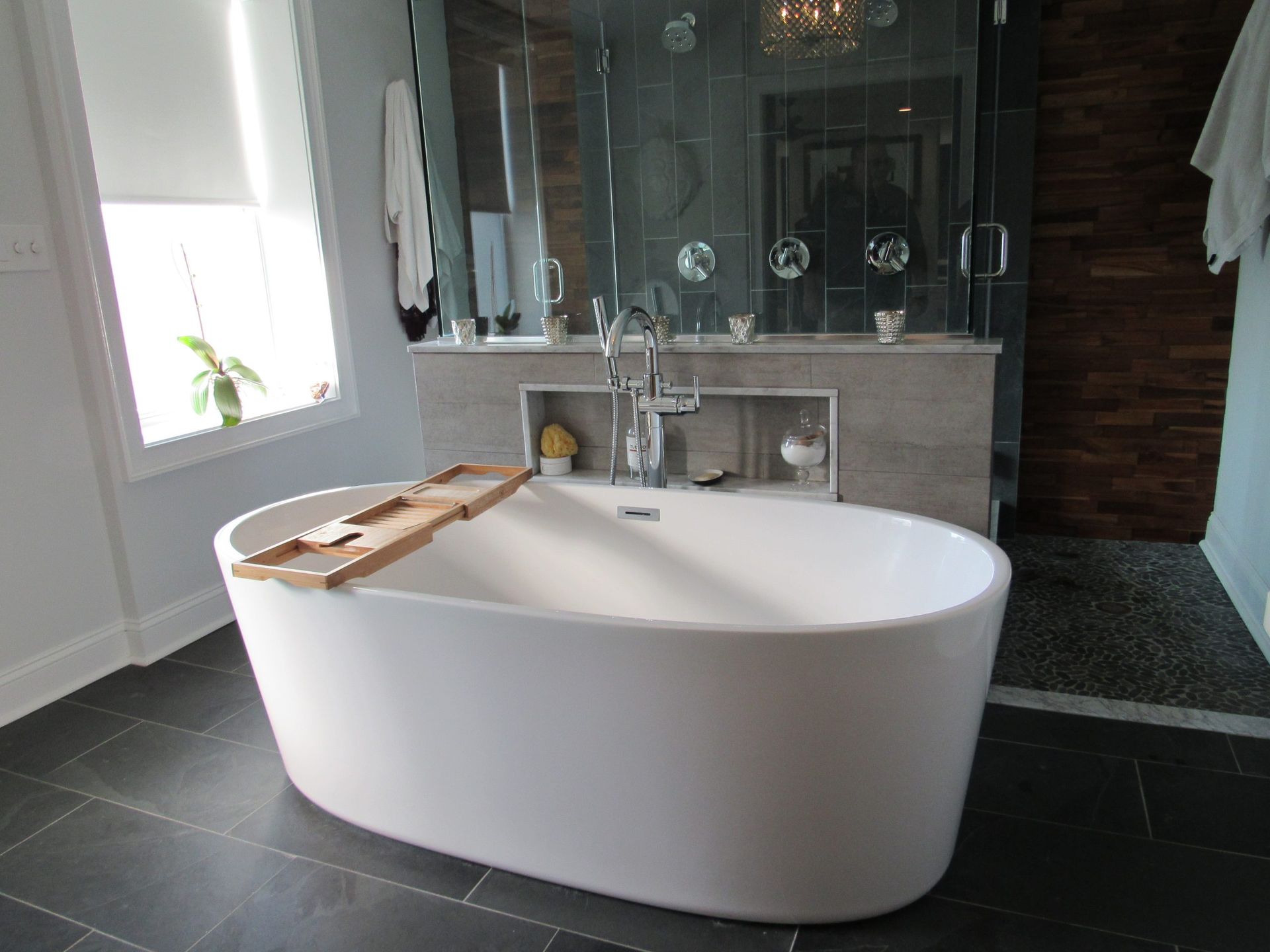 Modern bathroom with a white oval bathtub, stone tile floor, and a glass shower.