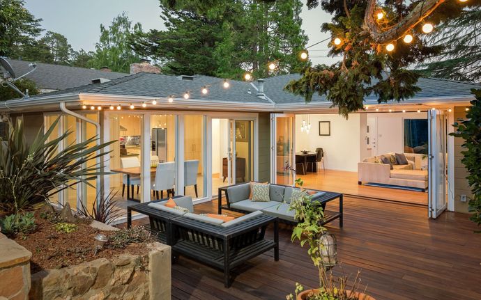Terrasse arrière avec foyer, sièges et portes vitrées ouvertes donnant sur l'intérieur de la maison ; guirlandes lumineuses.