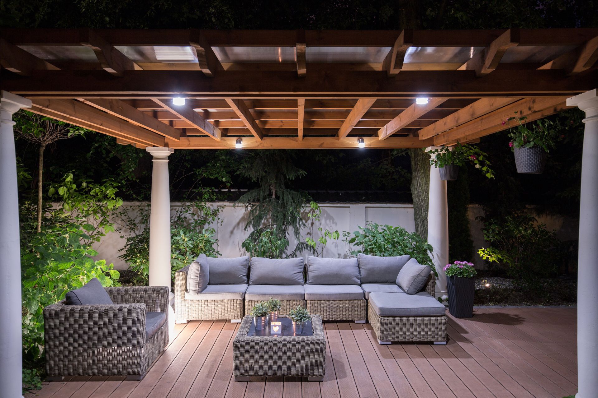 Terrasse extérieure avec mobilier en osier sous une pergola en bois, éclairée la nuit.