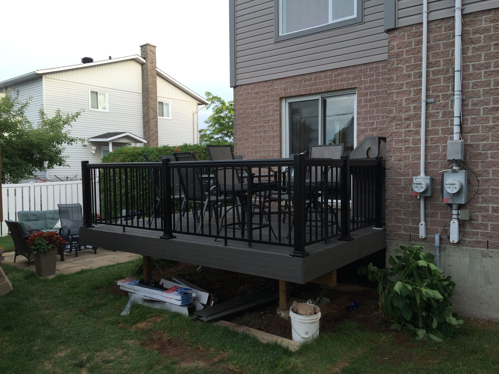 Une terrasse arrière avec une balustrade noire et du mobilier de jardin, jouxtant une maison en briques.