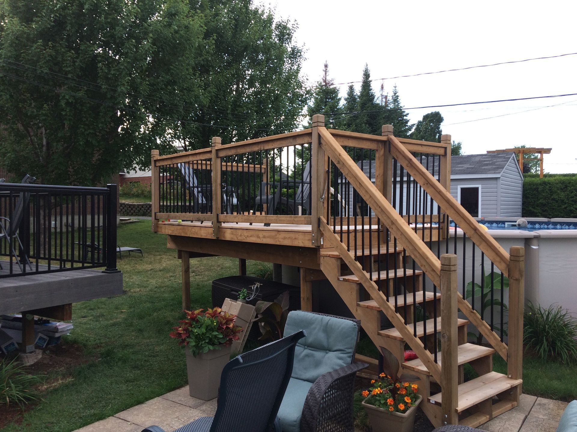 Terrasse en bois avec escalier et rambarde noire, donnant sur un jardin avec piscine.