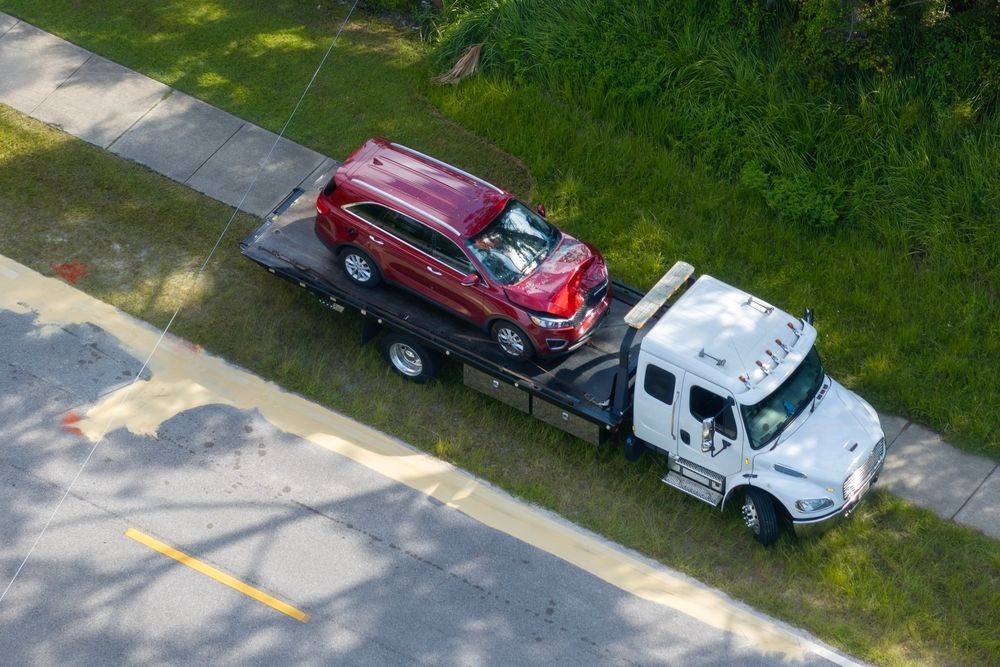 A red SUV with significant front-end damage is being transported on the back of a white flatbed tow truck.