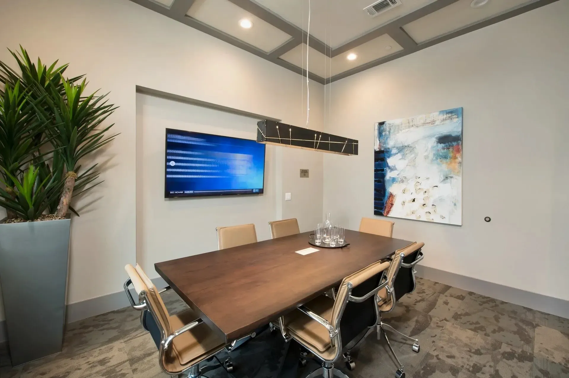 Modern conference room with a large table, chairs, TV, and decorative artwork.