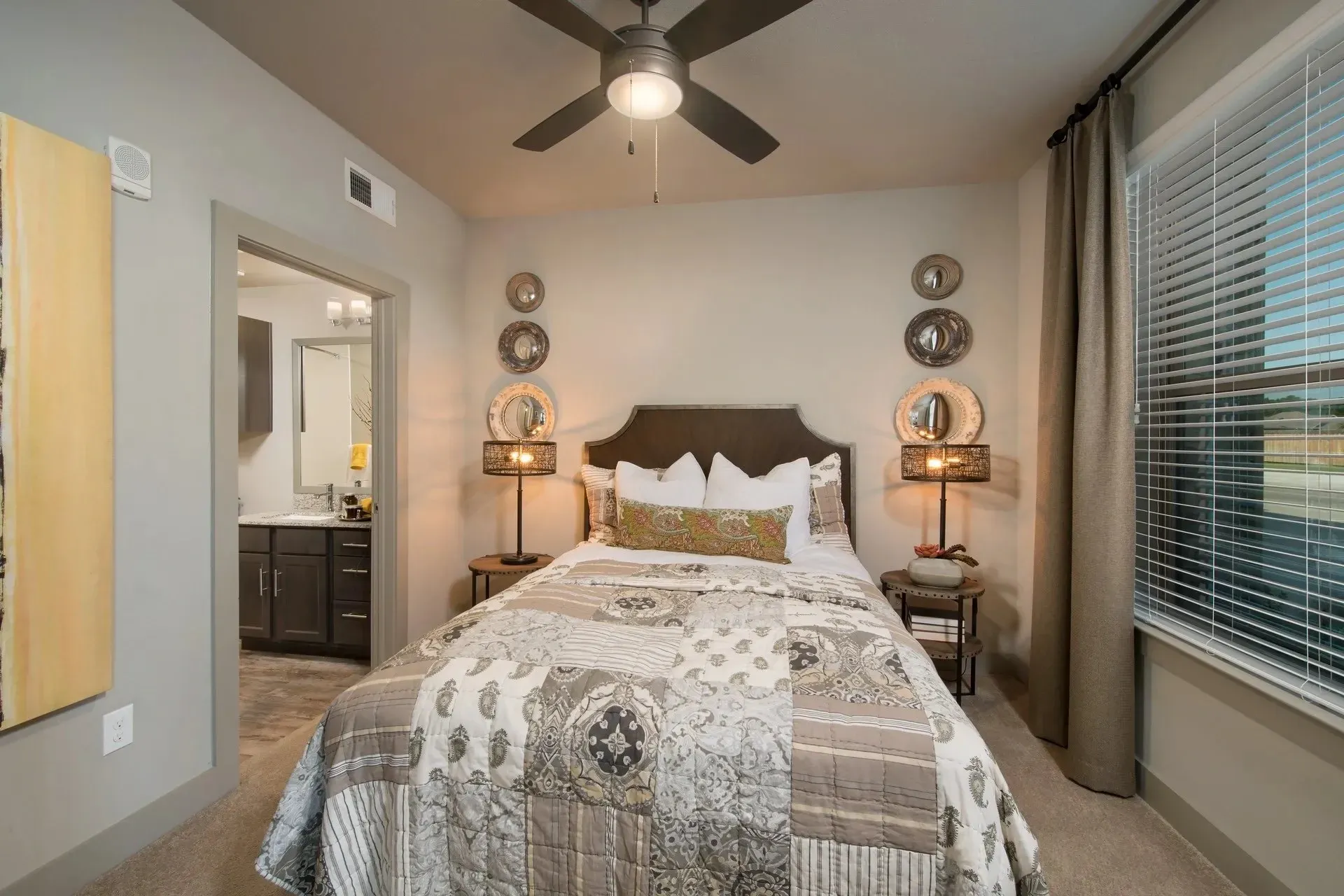Elegant bedroom with a queen-sized bed and decorative pillows, featuring wall decor and natural light through windows.