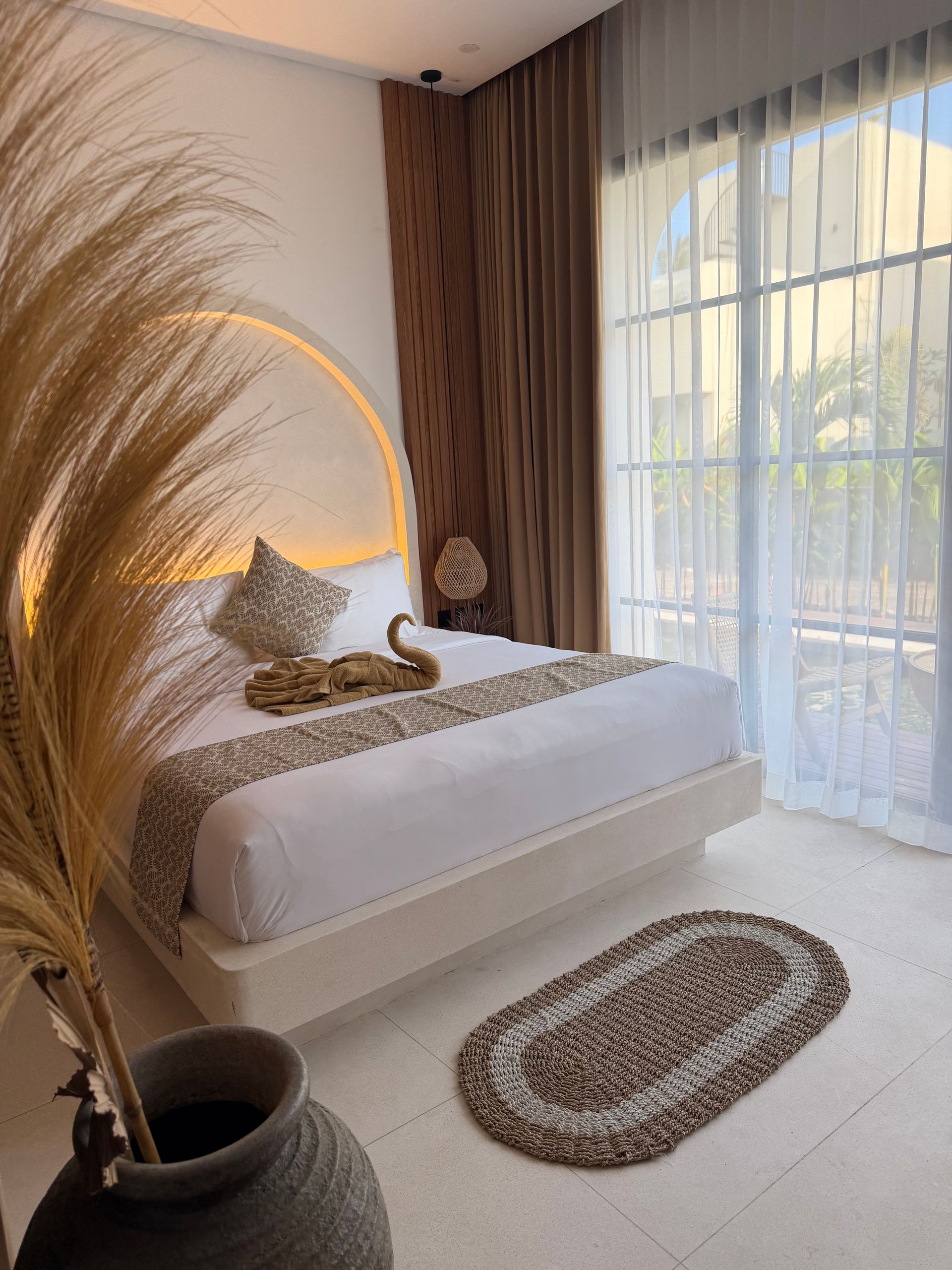 A bedroom with a bed, two gray pillows, one patterned pillow, two round wall art pieces, and a lamp on a small side table.