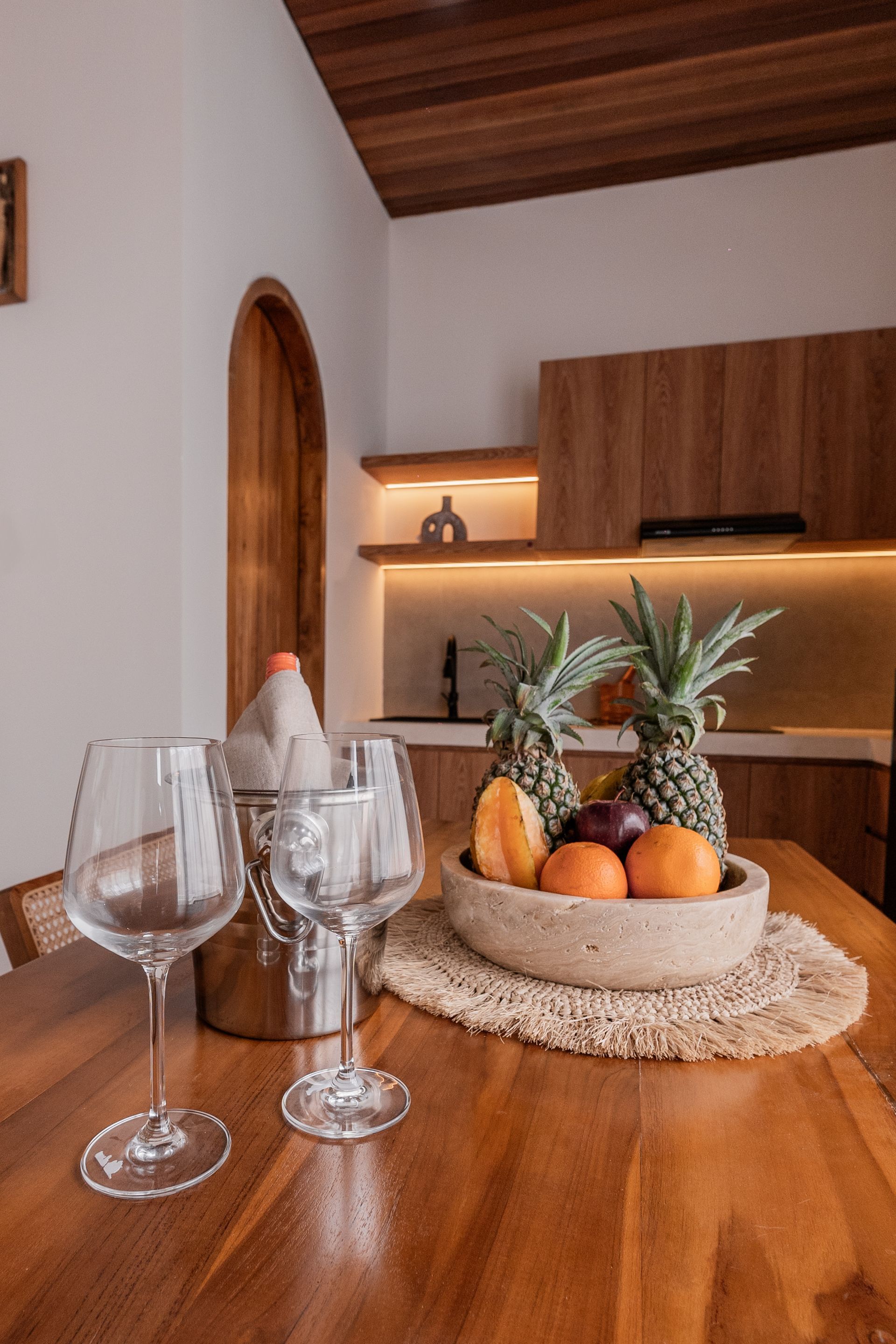 Wine glasses and a fruit bowl on a wooden table in a warm, modern kitchen