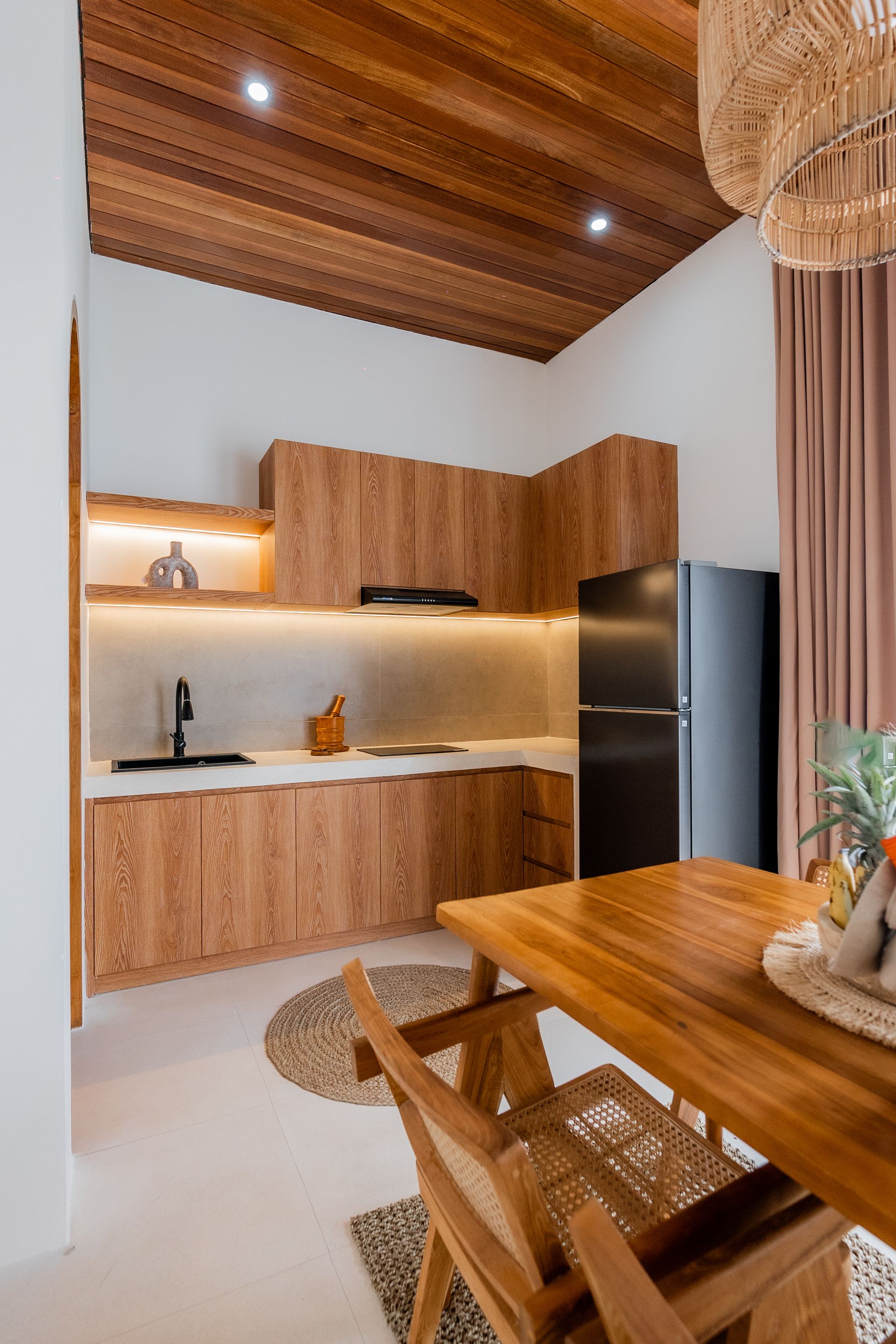 Modern kitchen and dining nook with wood cabinetry, black appliances, warm lighting, and a wooden table
