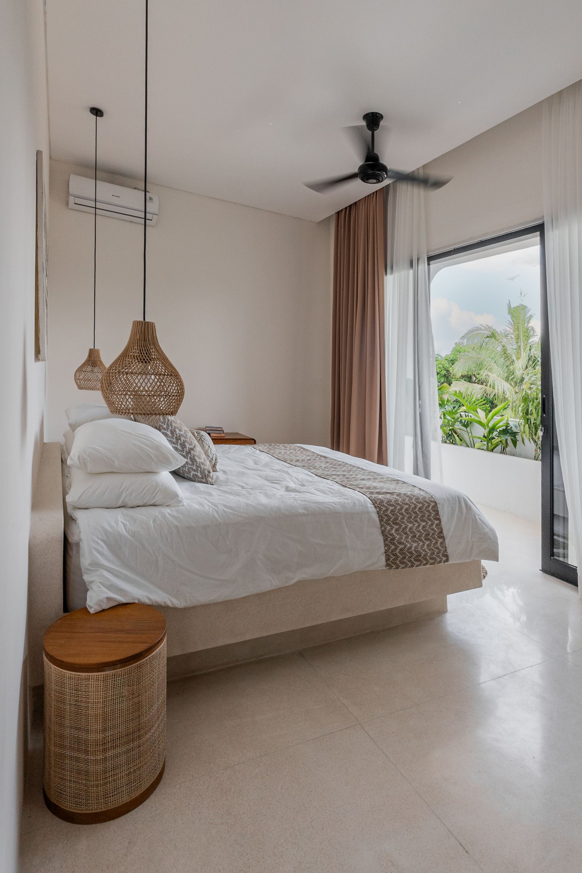 Bright minimalist bedroom with a hanging rattan chair, bed, and large window overlooking greenery.