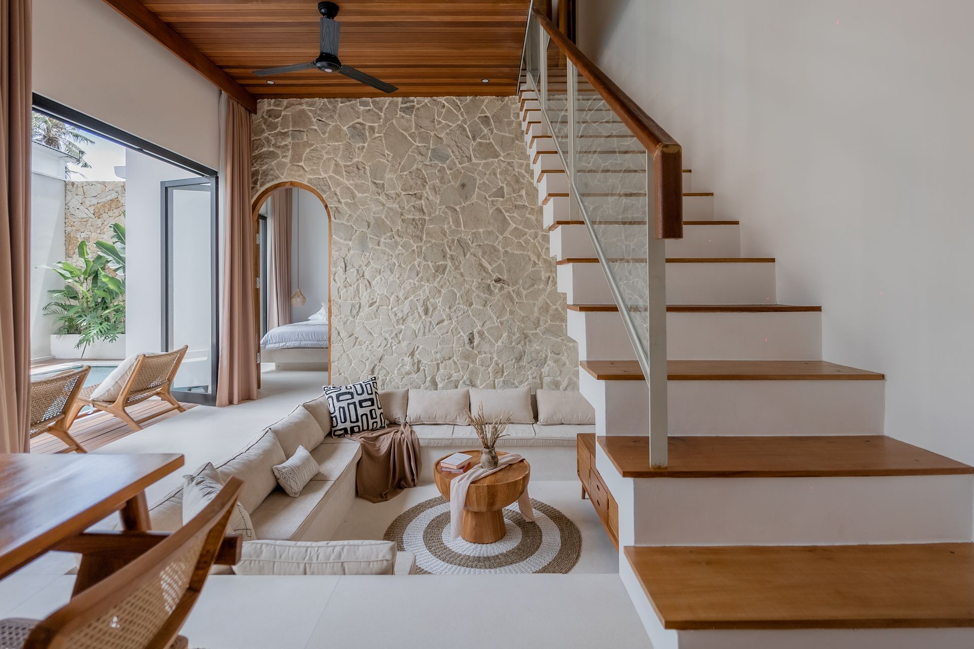 Modern living room with stone accent wall, staircase, and bohemian rug under a wooden loft ceiling