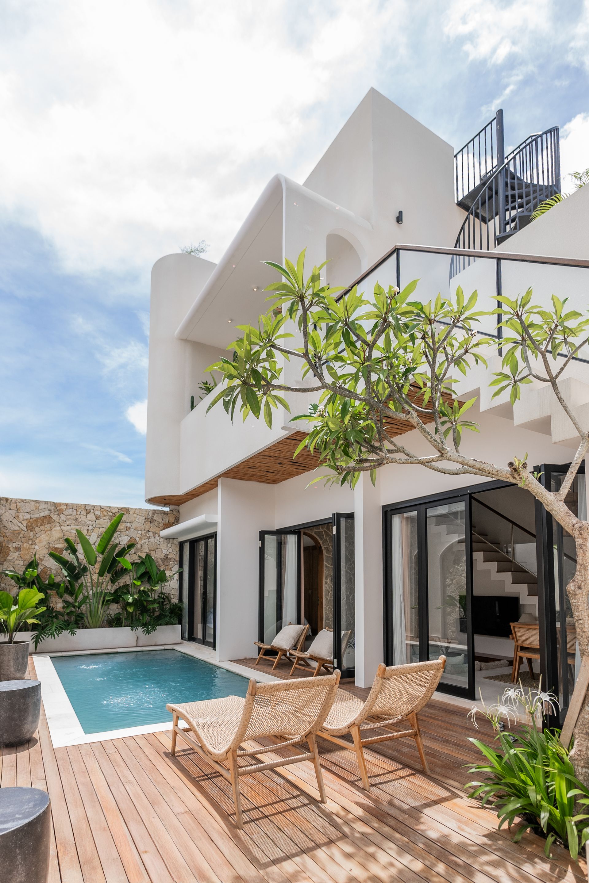 Modern white villa with pool, patio chairs, and sliding glass doors under a bright sky