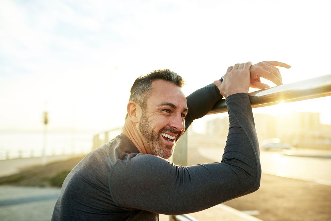 Smiling man in athletic wear stretching with a club at sunrise outdoors