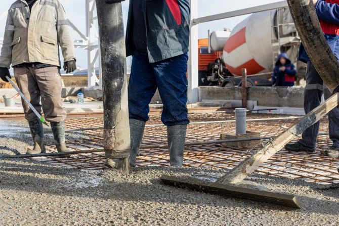 Workers pouring concrete at a construction site, with a cement mixer truck in the background.