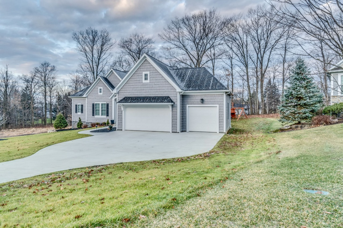 Gray suburban house with two-car garage and a curved driveway on a grassy lot.