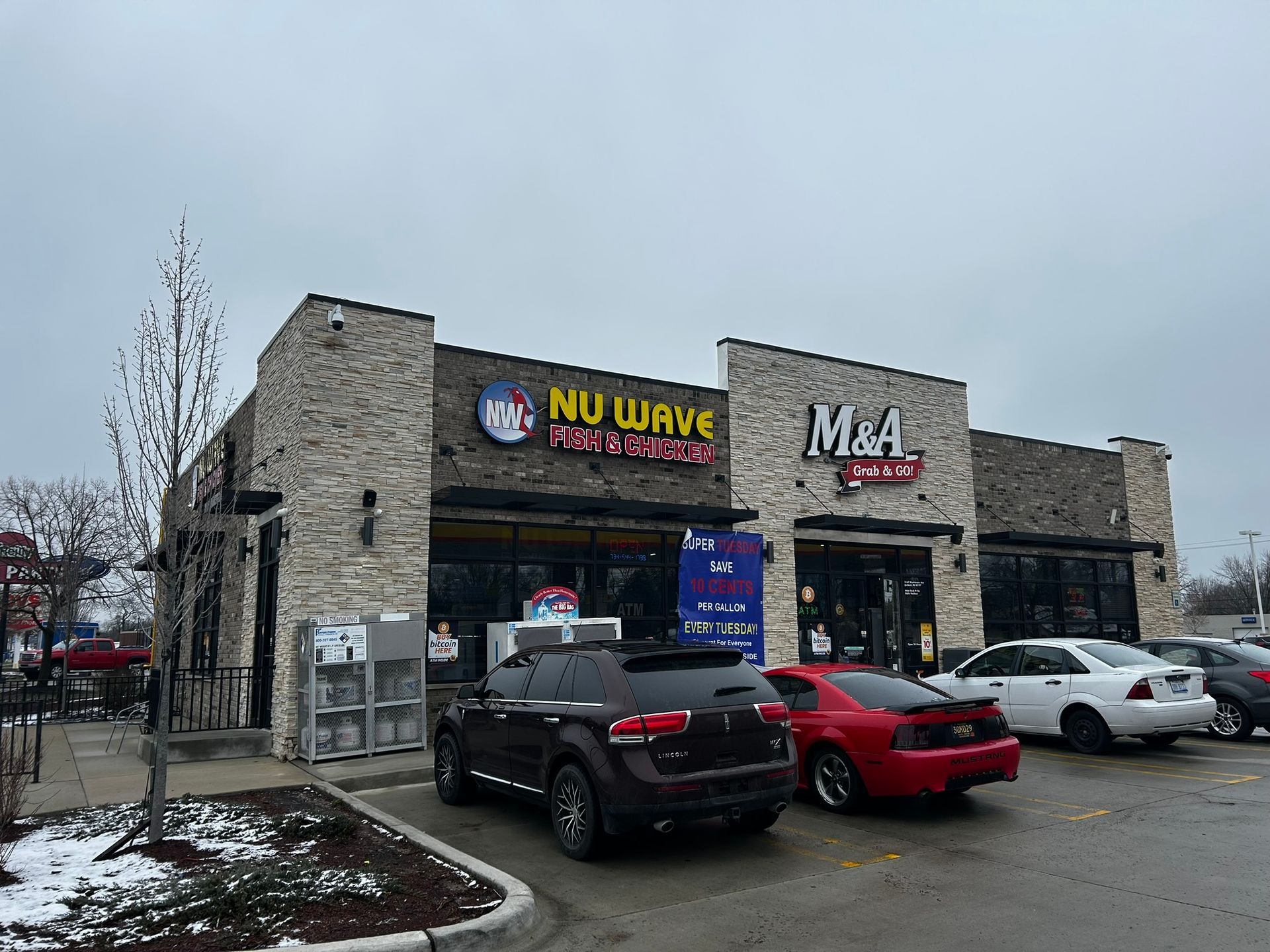 Stone strip mall storefront with NU WAVE and M&A signs, parked cars, and patches of snow