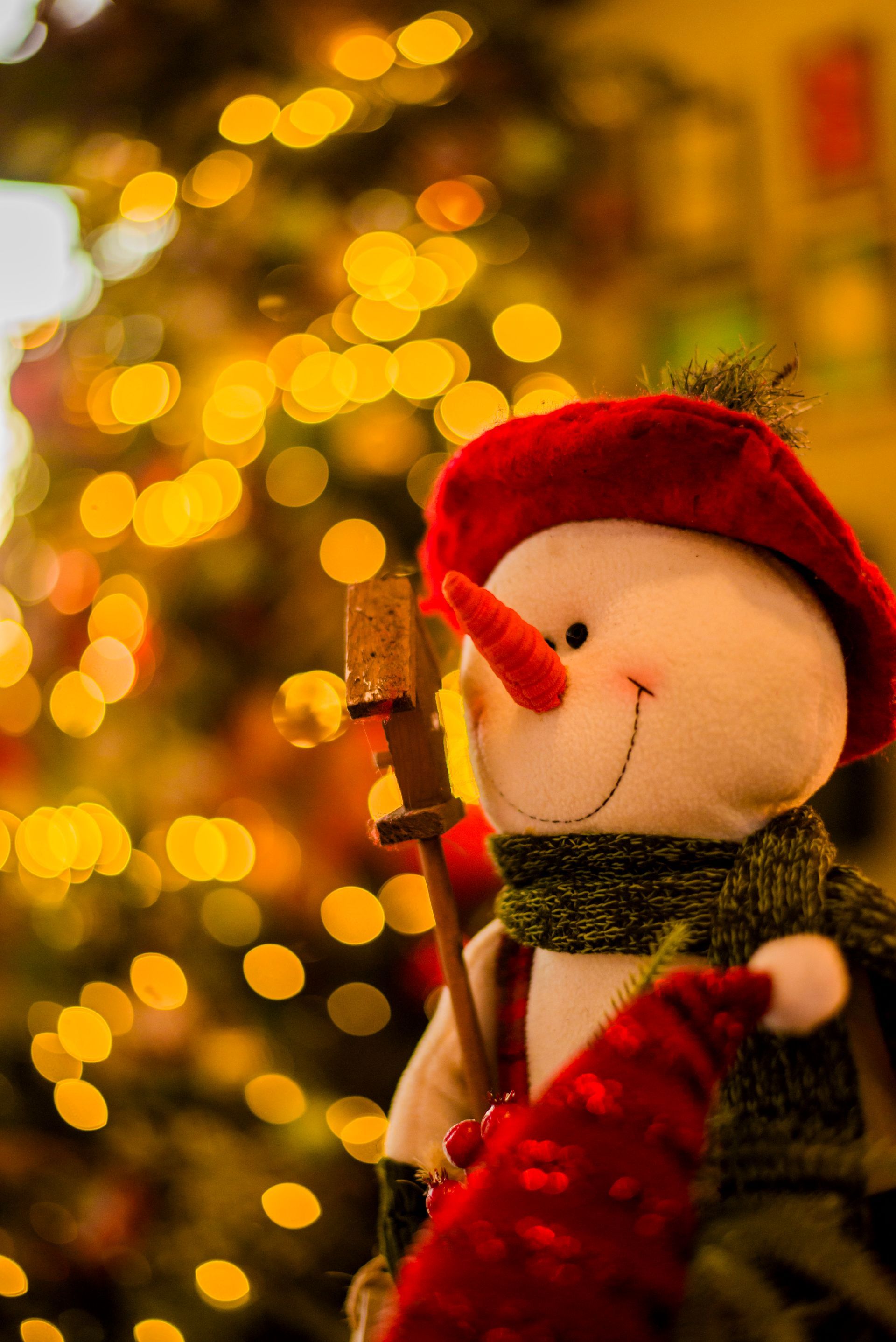 Um boneco de neve de pelúcia está parado em frente a uma árvore de natal.