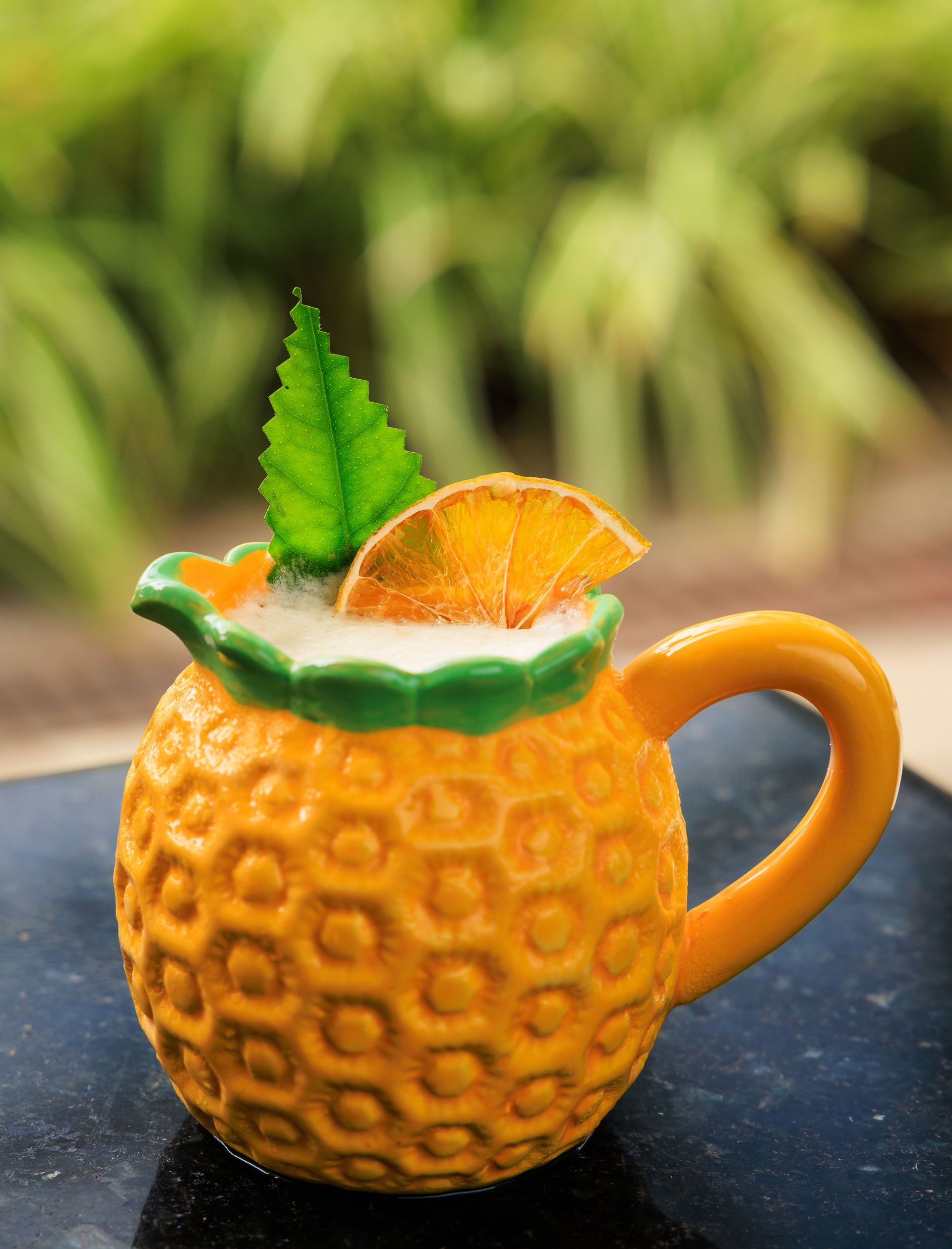 Uma caneca em formato de abacaxi cheia de uma bebida e uma fatia de laranja.