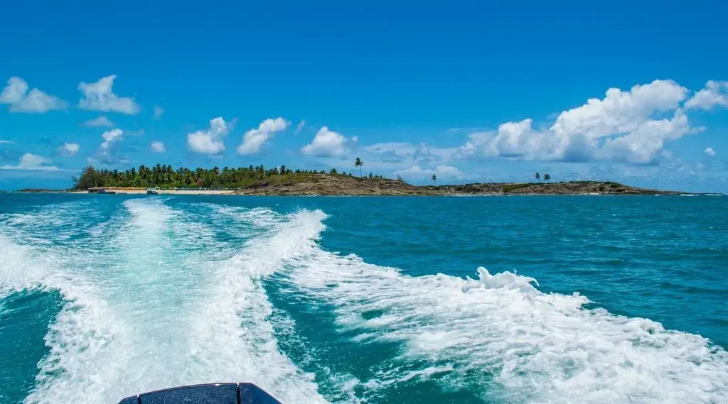 Um barco está navegando pelo oceano em direção a uma pequena ilha.
