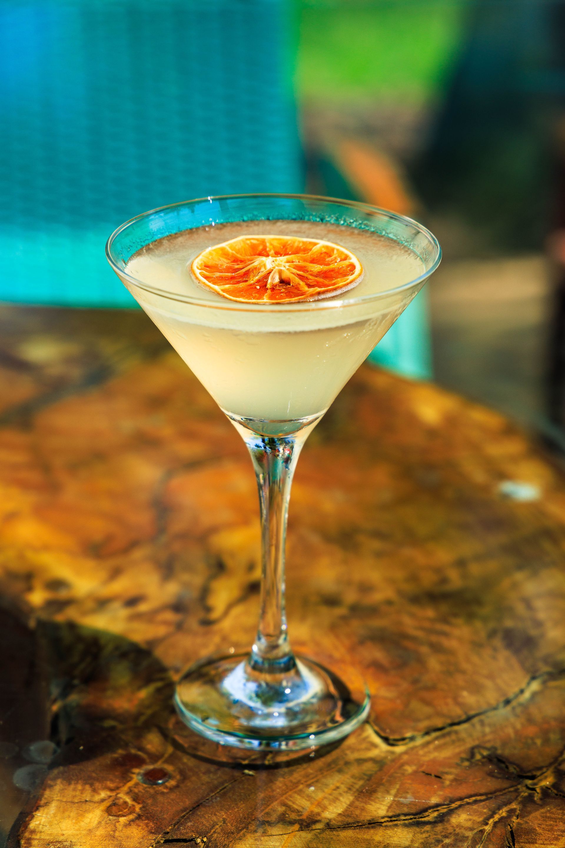 Uma taça de martini cheia de um líquido branco e uma fatia de laranja sobre uma mesa de madeira.