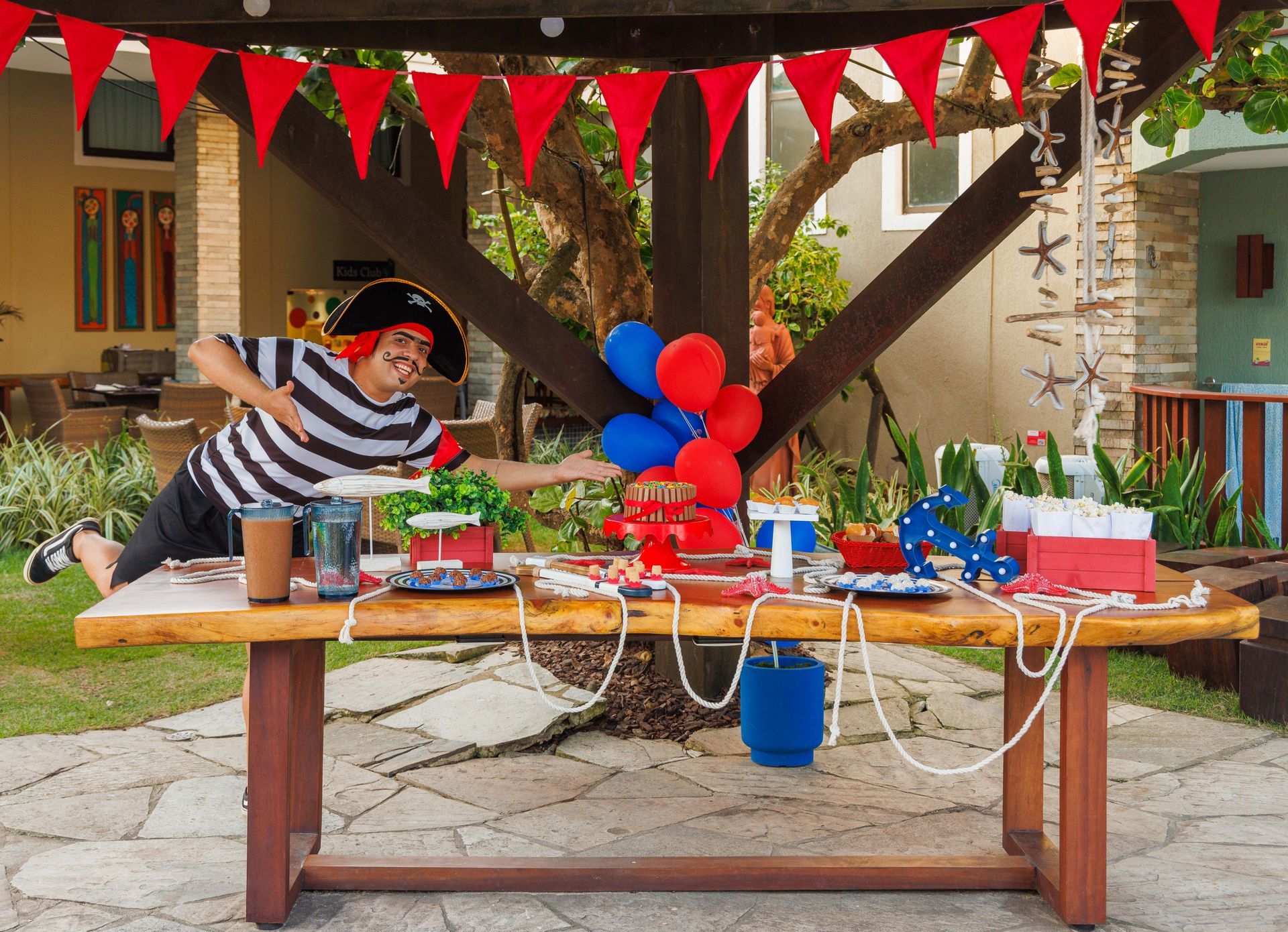 Um homem vestido de pirata está em pé em frente a uma mesa decorada para uma festa pirata