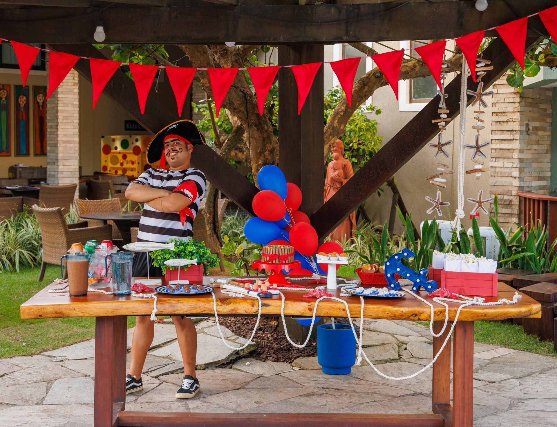 Um homem vestido de pirata está em pé em frente a uma mesa decorada para uma festa pirata.
