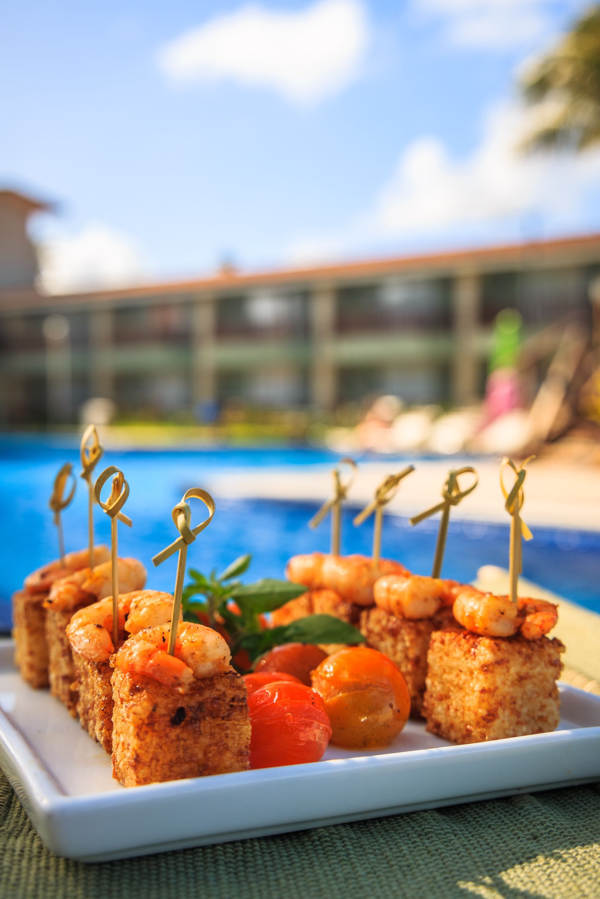 Um prato de comida com camarão e tomates em palitos de dente em frente a uma piscina.