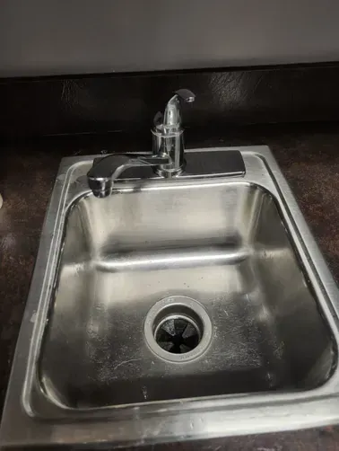 Stainless steel kitchen sink with faucet and drain, viewed from above.