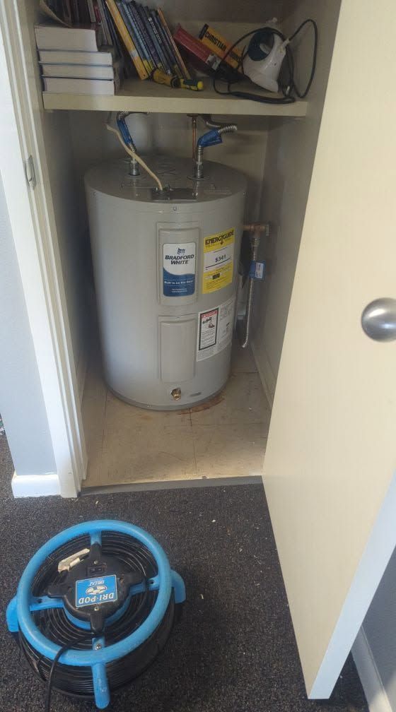 Open closet with a white water heater; blue circular device on the floor in front.