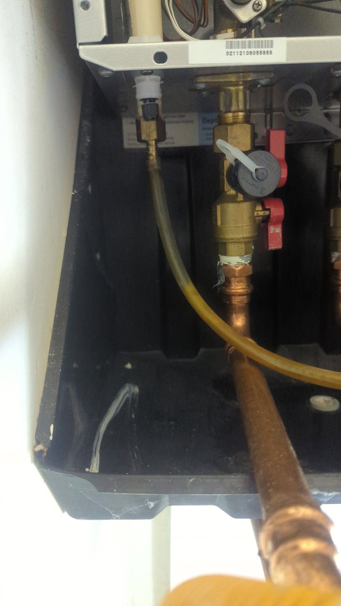 Close-up of a boiler’s internal plumbing with brass fittings, red valve handle, and copper pipe.