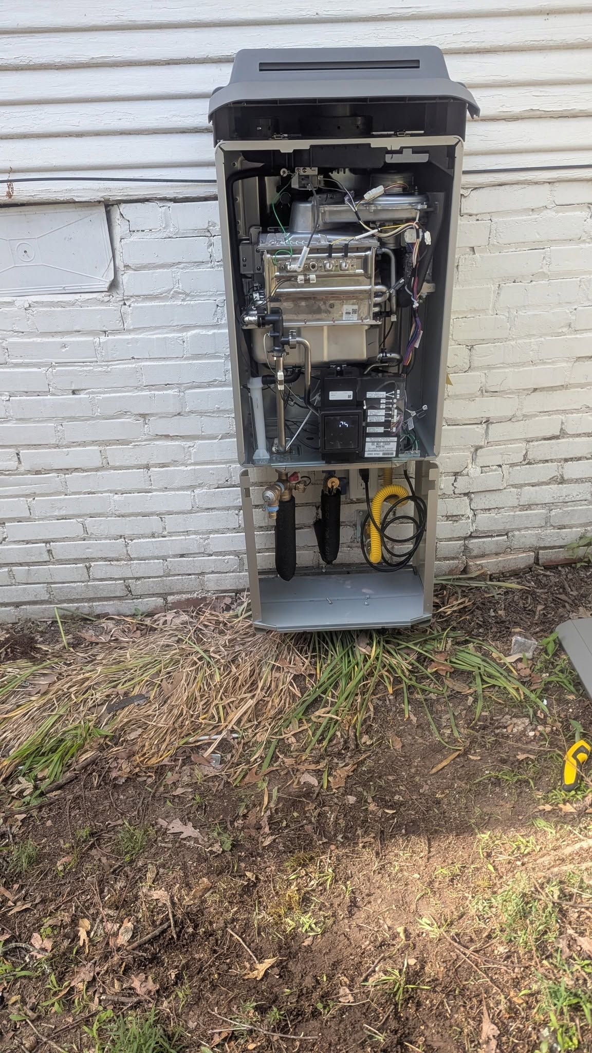 Open utility electrical cabinet with exposed wiring beside a white brick wall outdoors.