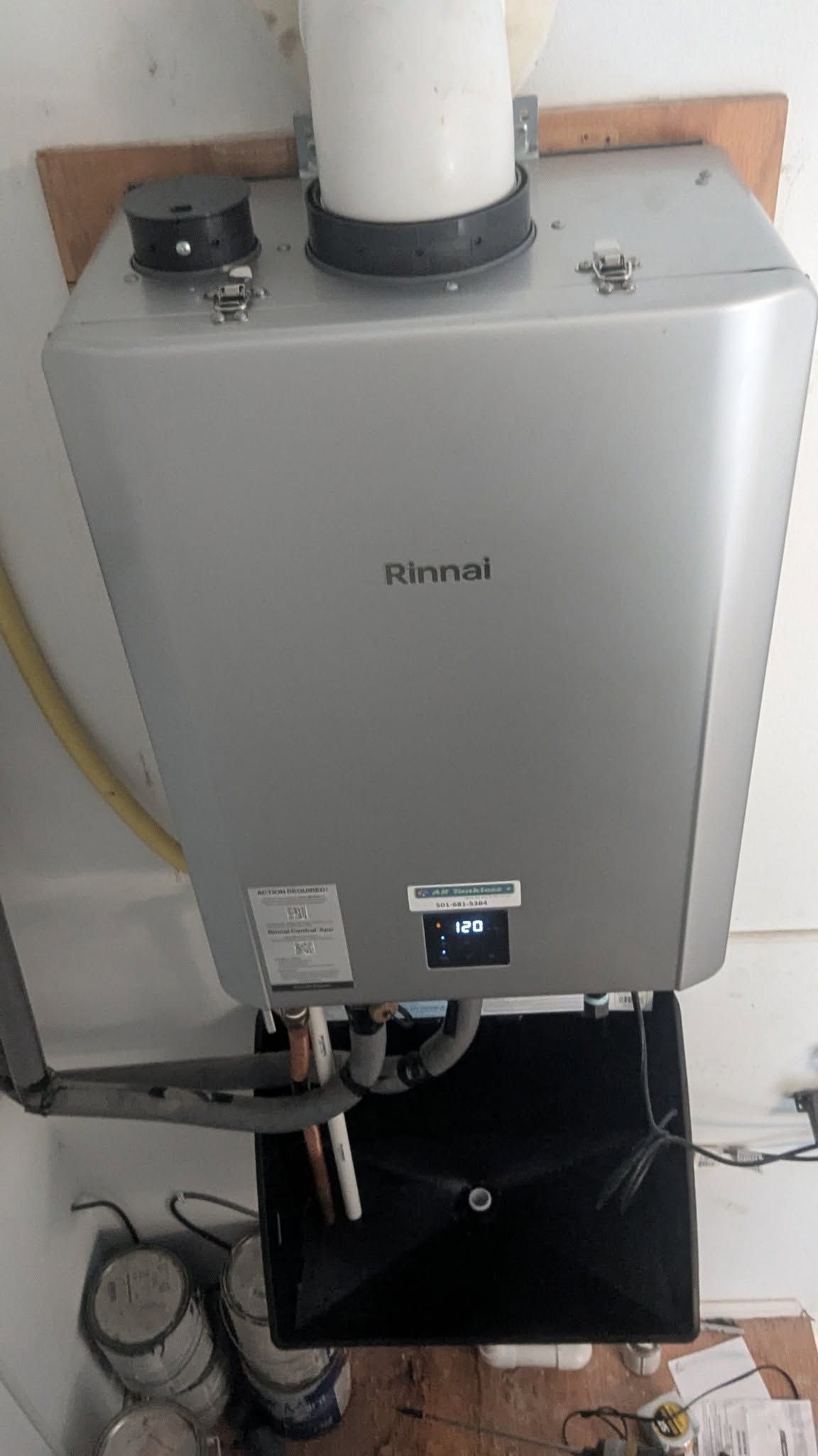 Wall-mounted silver boiler or water heater with pipes and vent, installed indoors against a white wall.