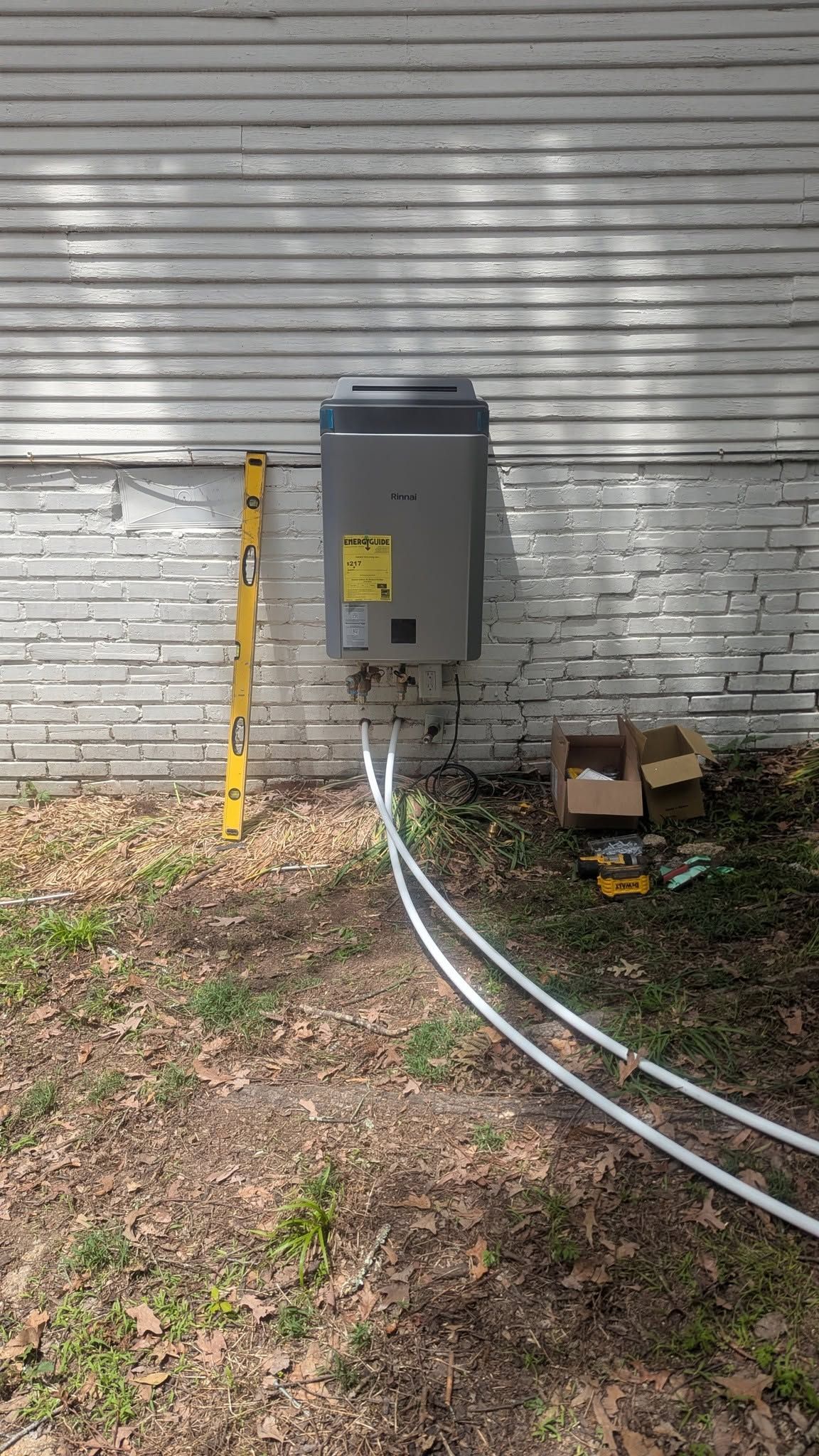 Gray electrical meter box on a weathered exterior wall with cables running below it.