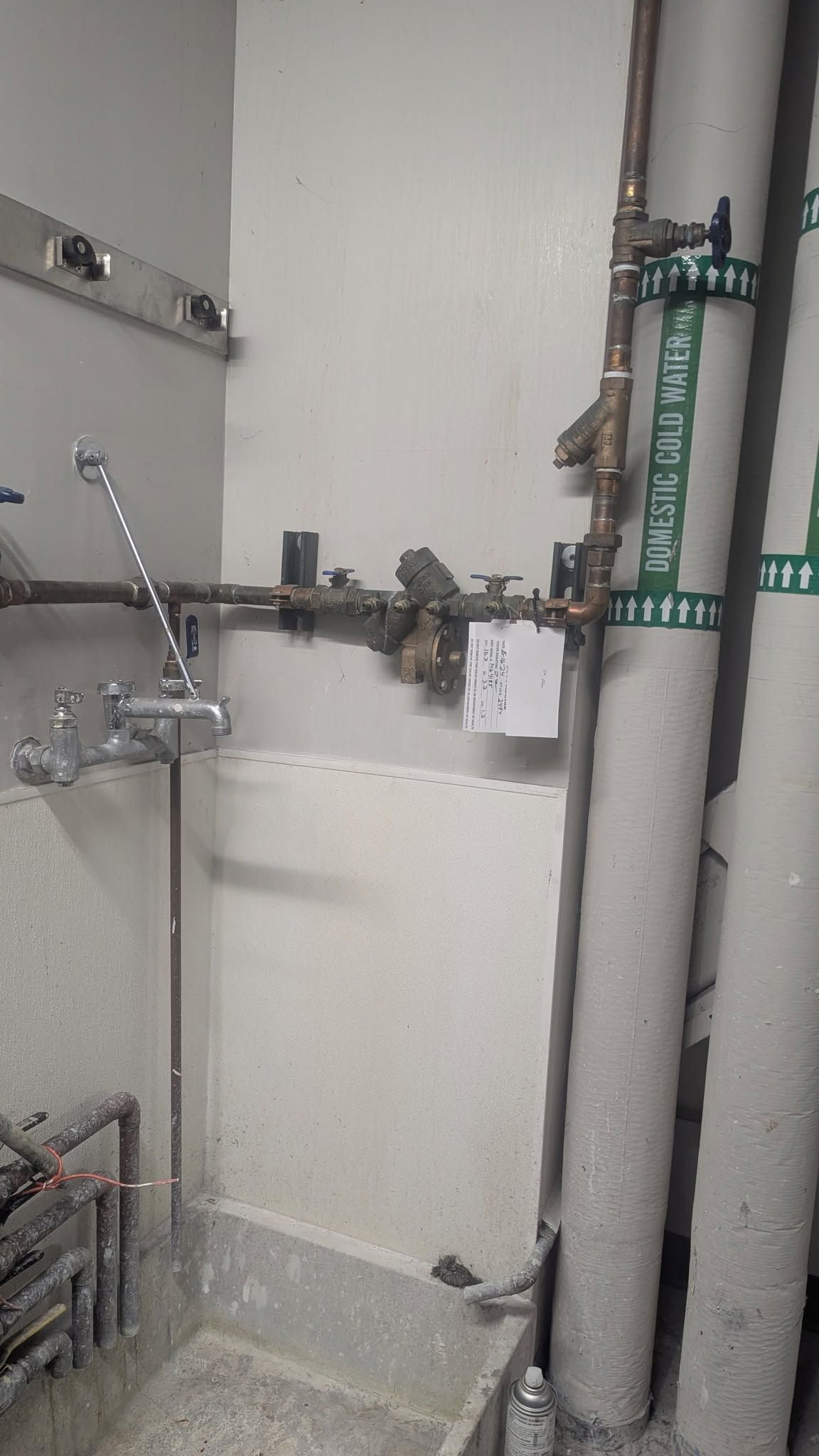 Utility room wall with exposed pipes, valves, and plumbing connections.