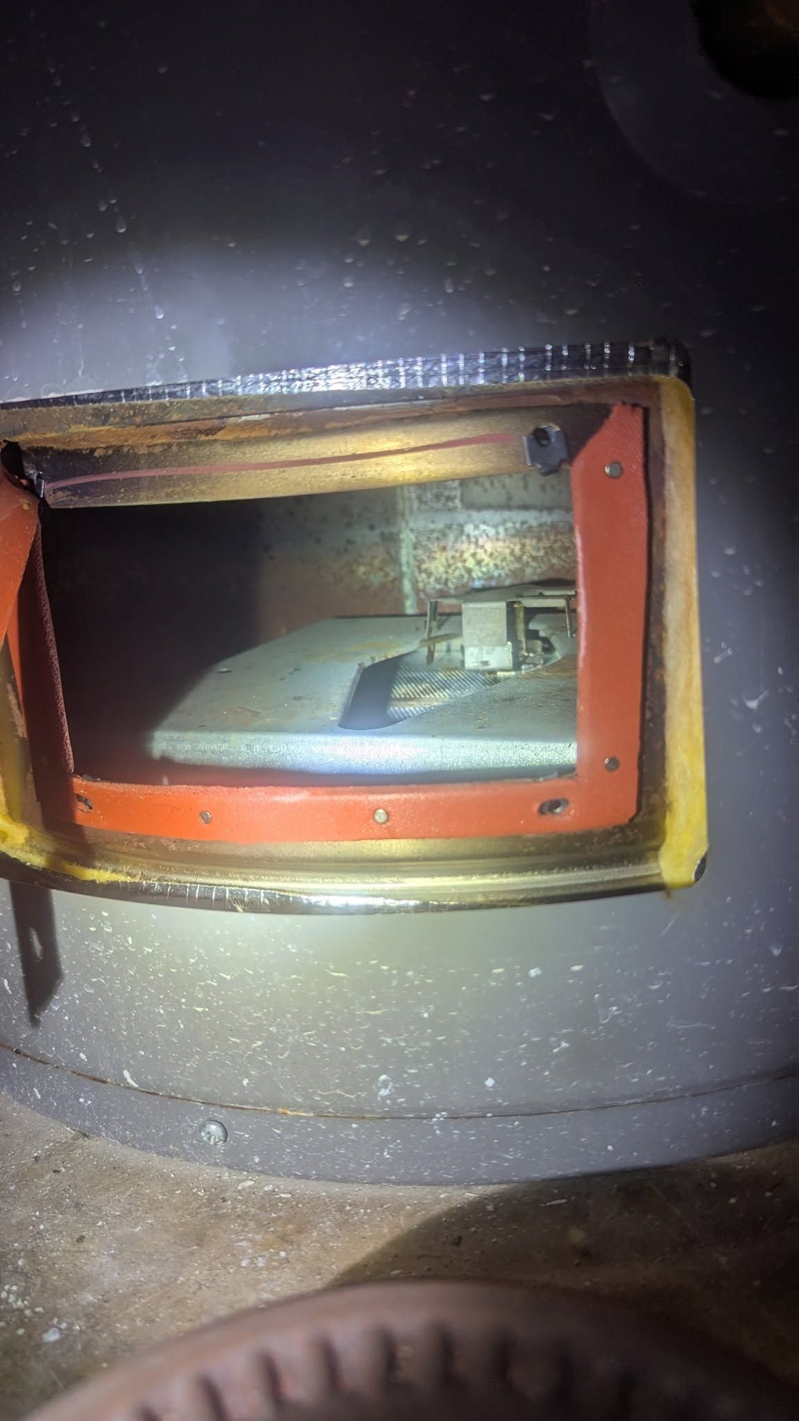 Close-up of a round metal oven door with a small orange-framed viewing window.