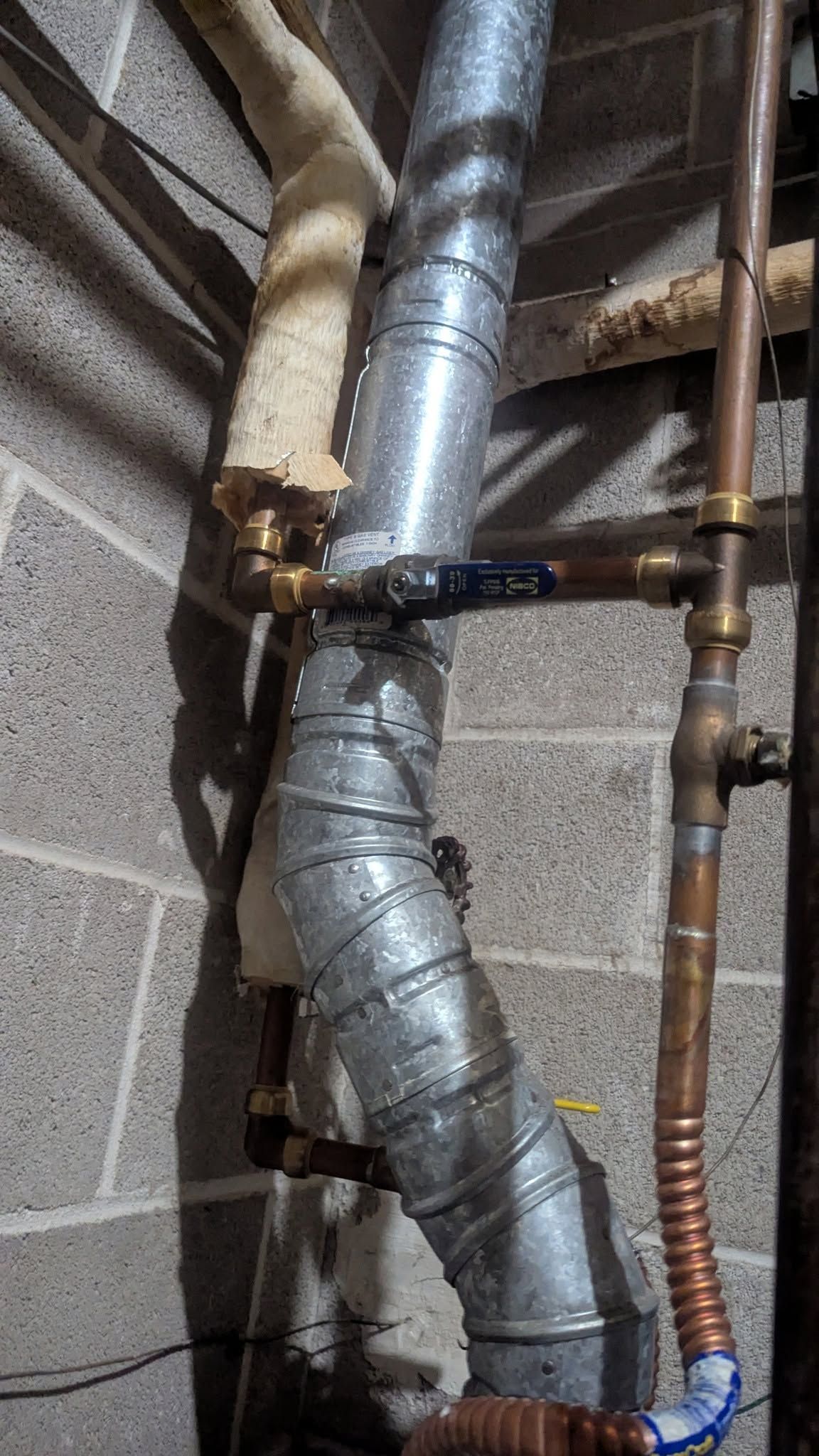Exposed basement pipes wrapped in silver insulation beside a cinder block wall.