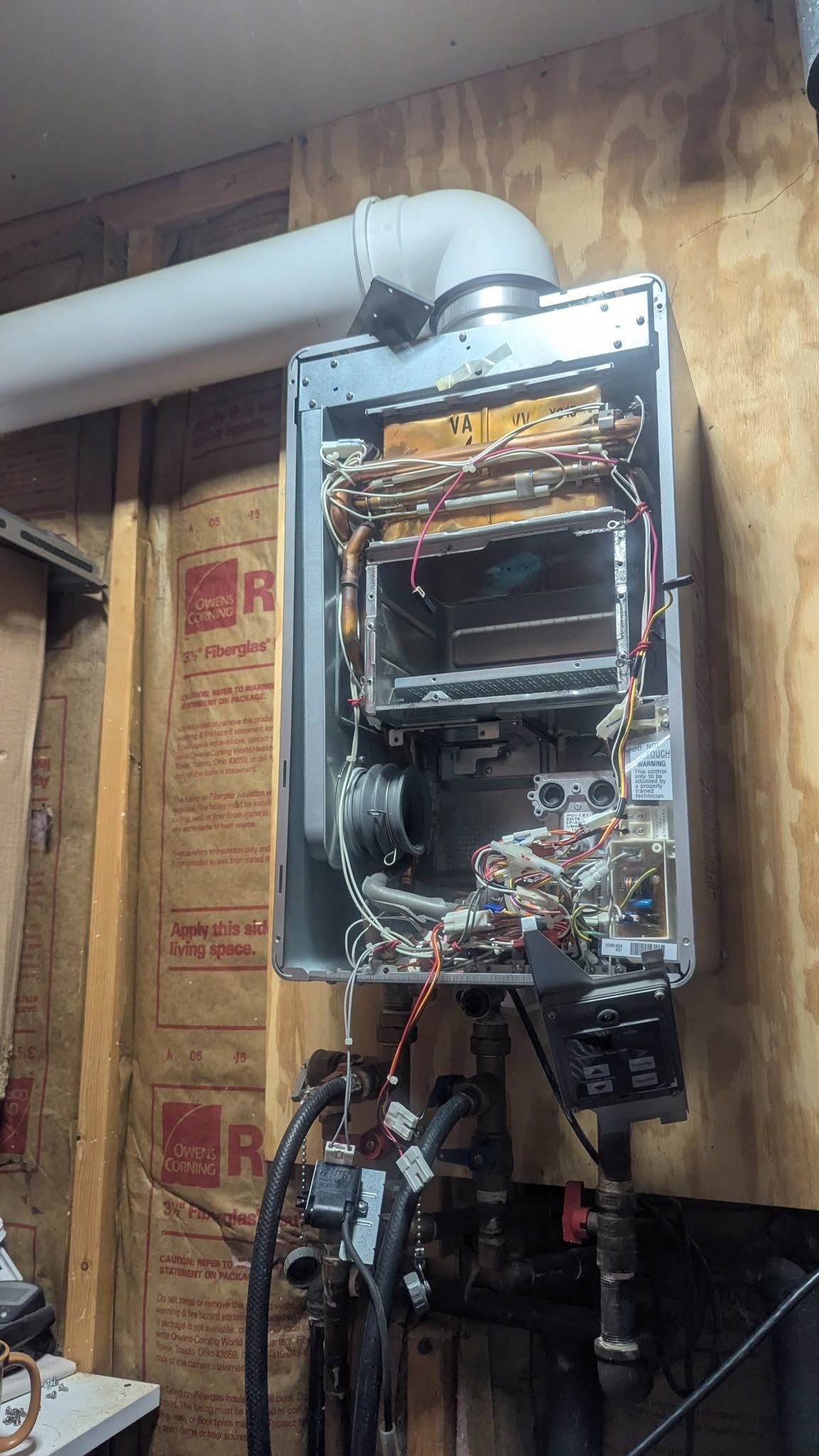 Open furnace cabinet with exposed wires and components on a basement wall