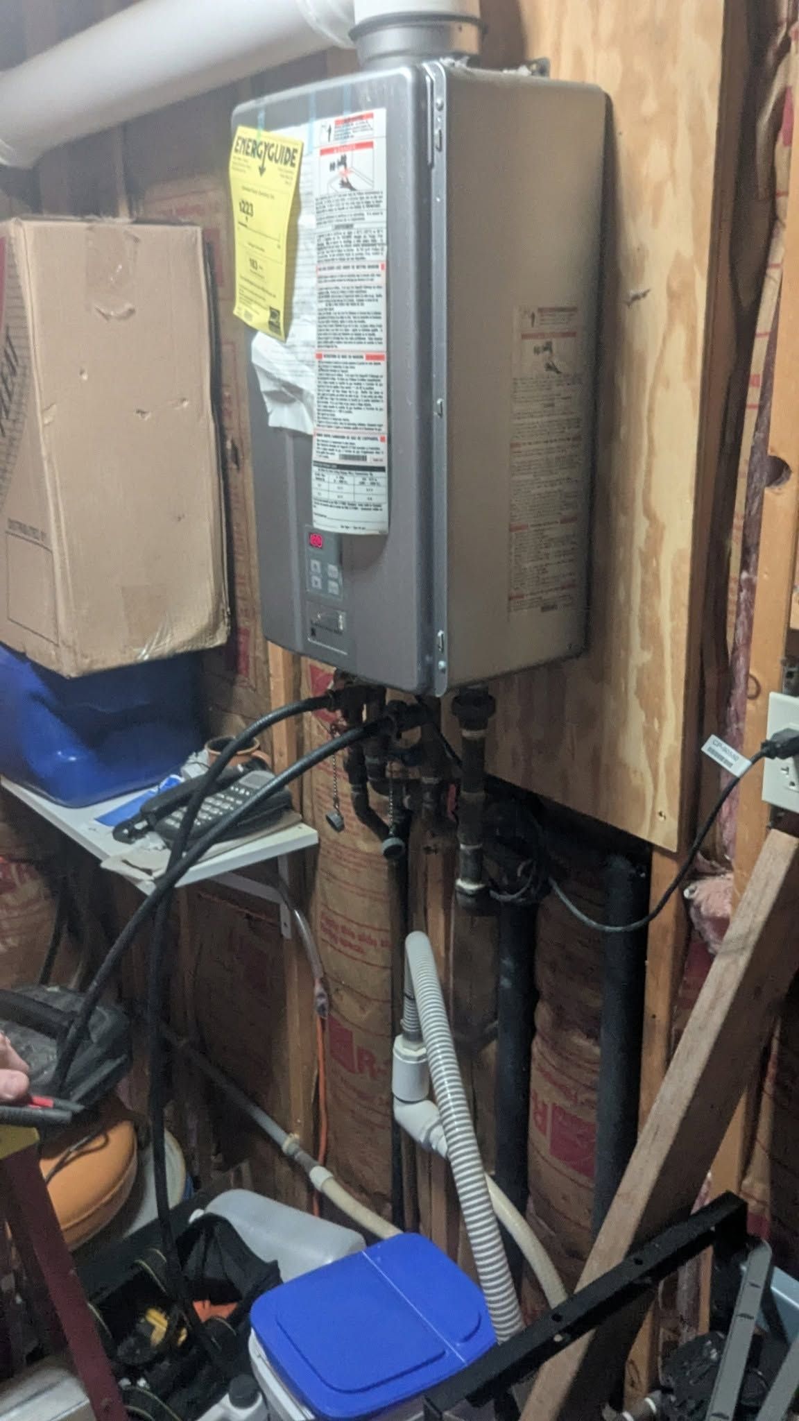 Wall-mounted electrical panel with labels and exposed wiring in a cluttered utility space