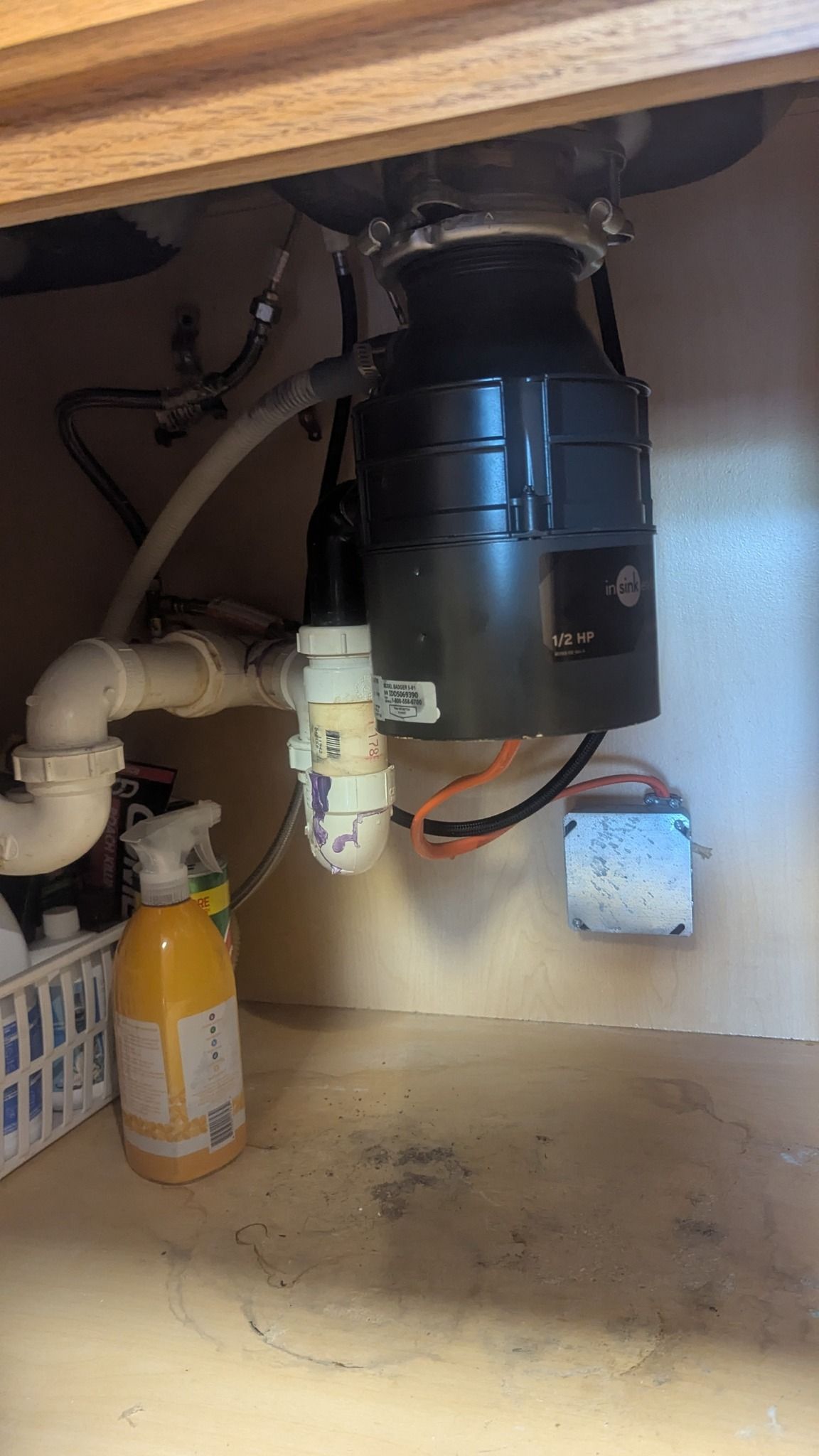 Under-sink garbage disposal and plumbing with cleaning supplies on the cabinet floor