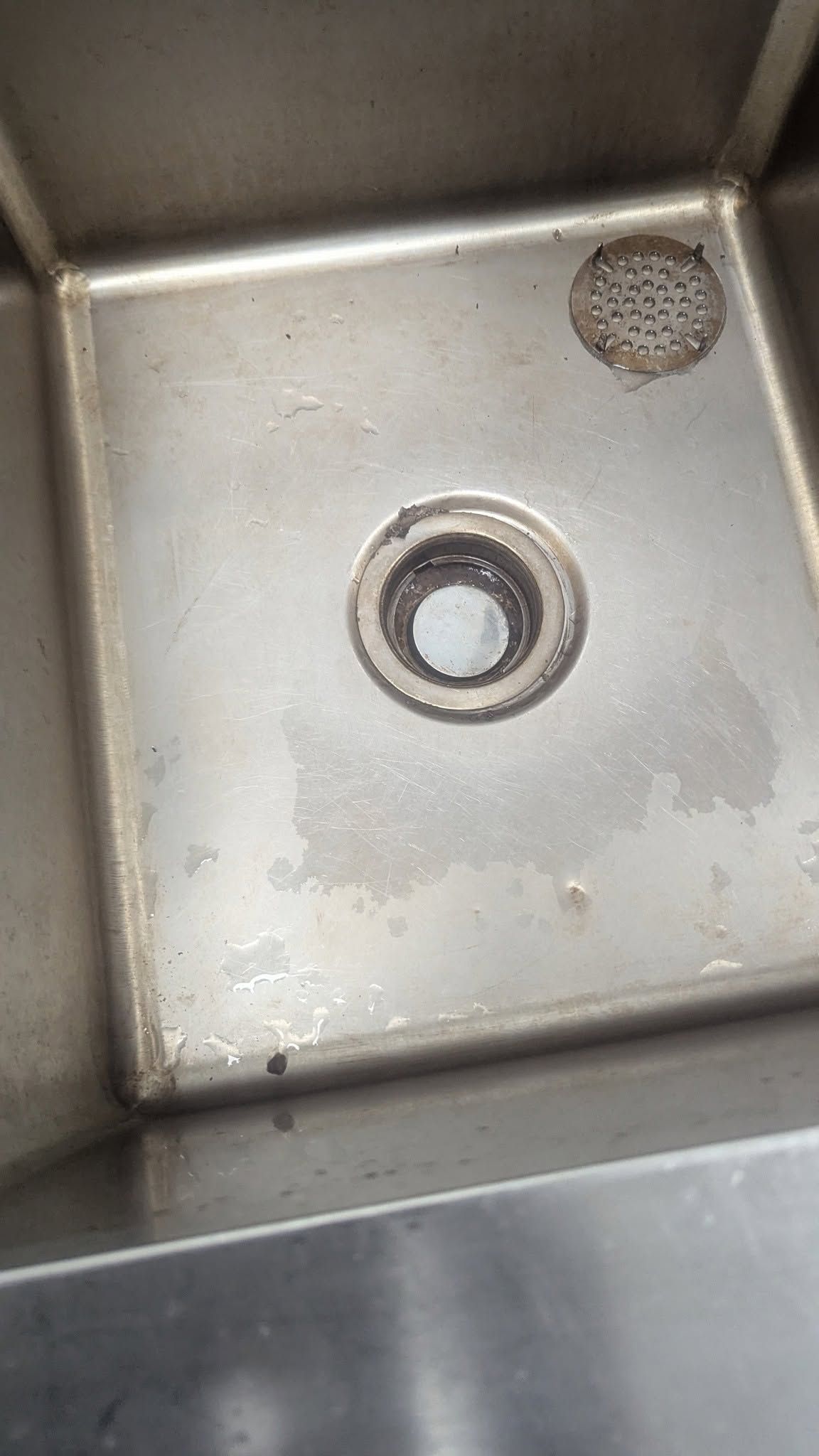 Stainless steel sink basin with a drain and a small debris-filled strainer in the corner.
