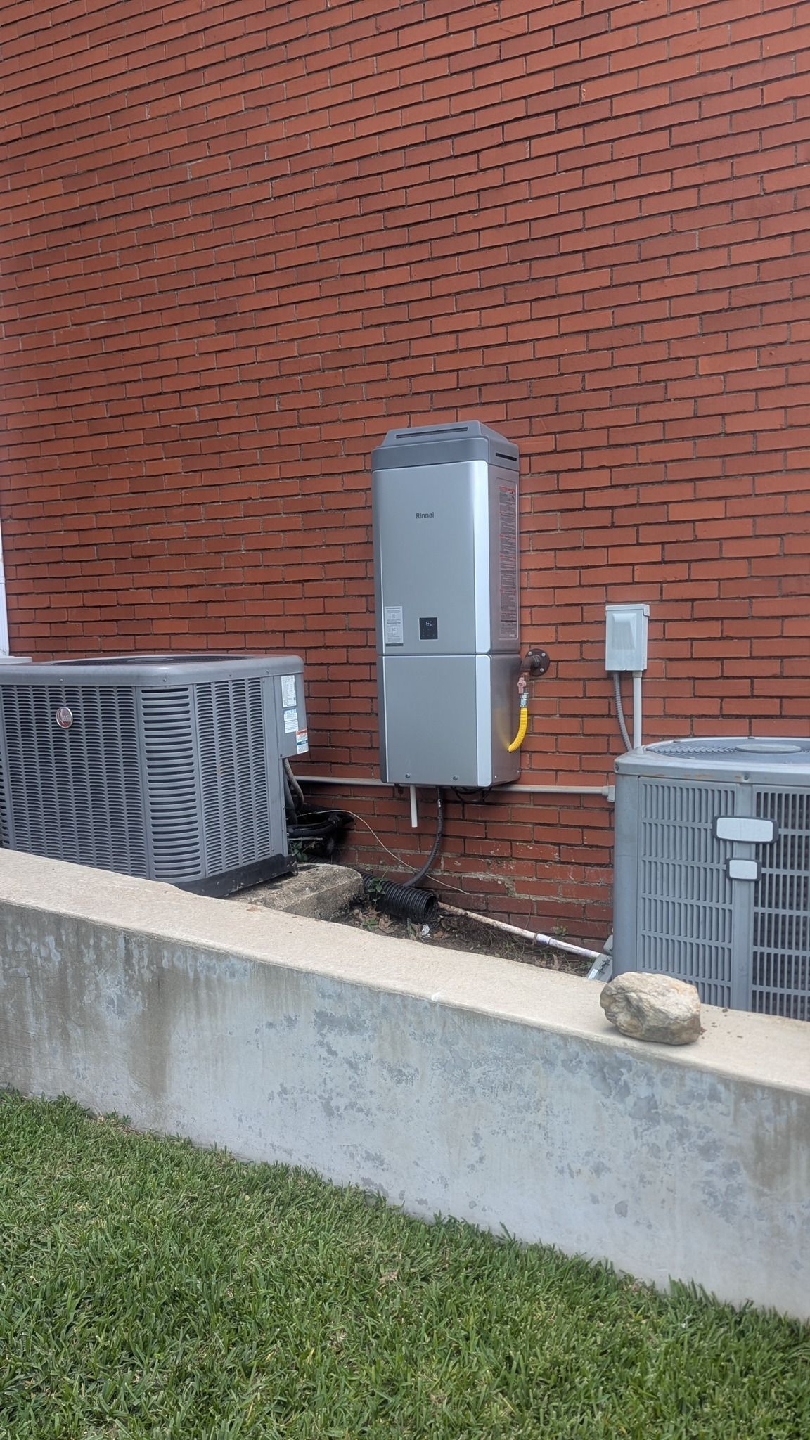 HVAC units mounted on brick building exterior. Includes an air conditioner, water heater, and electrical box.