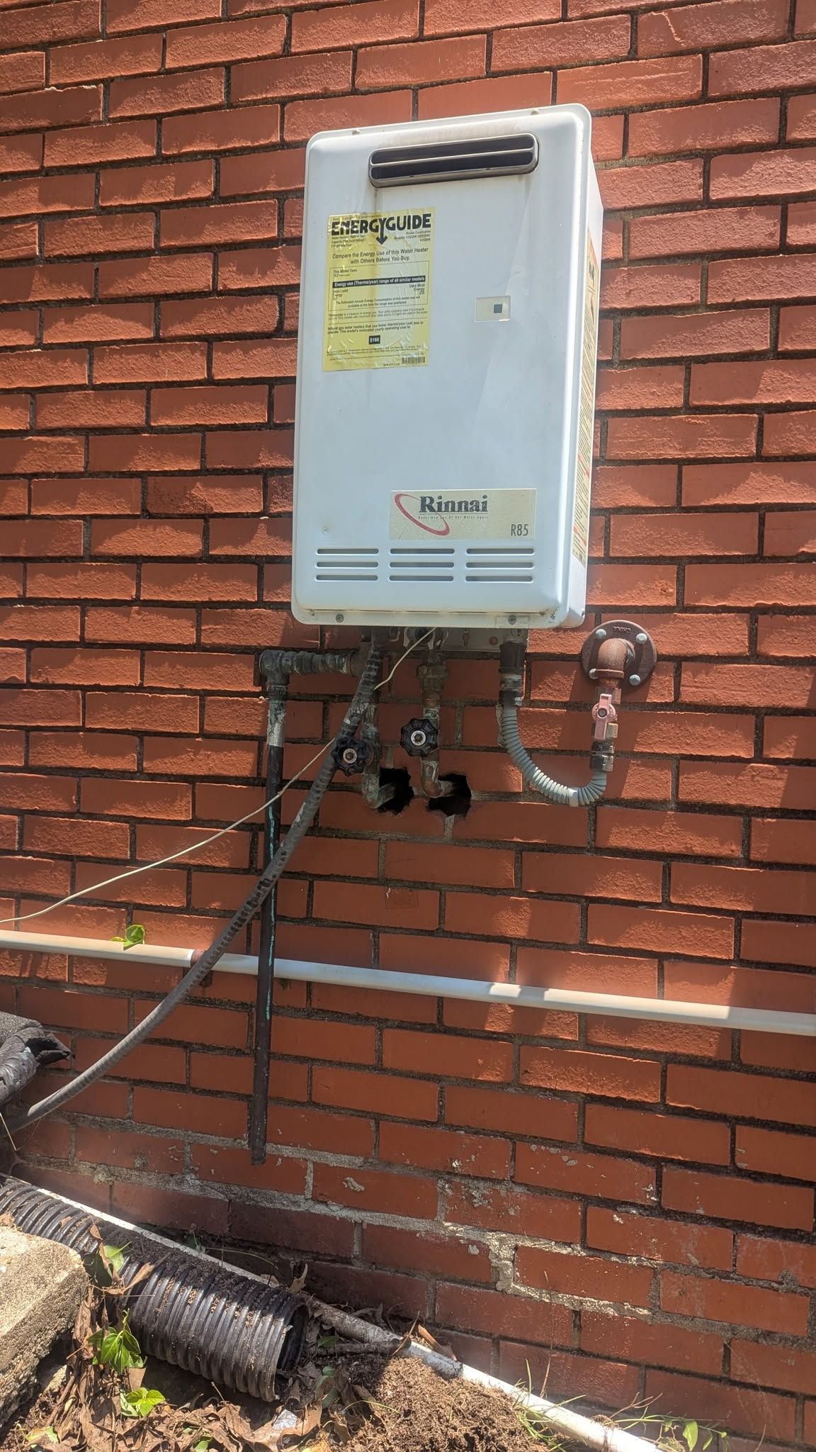 White utility box with pipes and meters mounted on a red brick wall outdoors